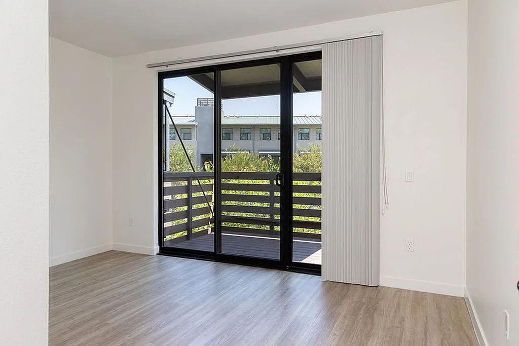 Bright and airy apartment bedroom featuring large sliding glass doors leading to a private balcony with charming views.