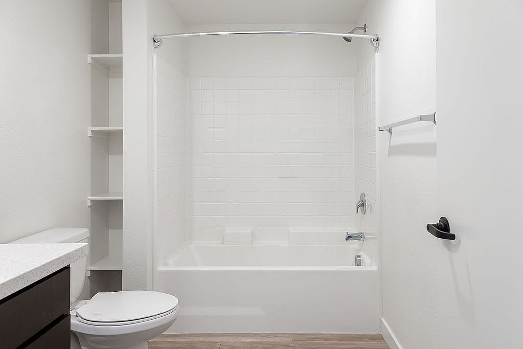 Bright and modern bathroom featuring a sleek white bathtub, elegant tiling, and ample shelving space.