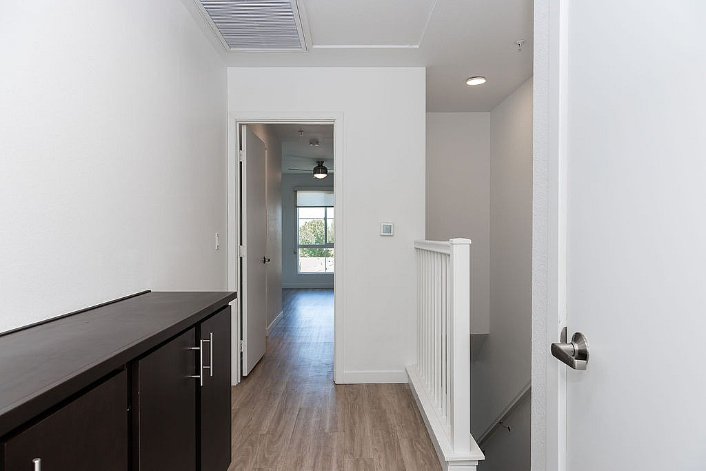 Bright and inviting hallway with sleek wooden flooring leading to a sunlit room, featuring modern design and ample natural light.