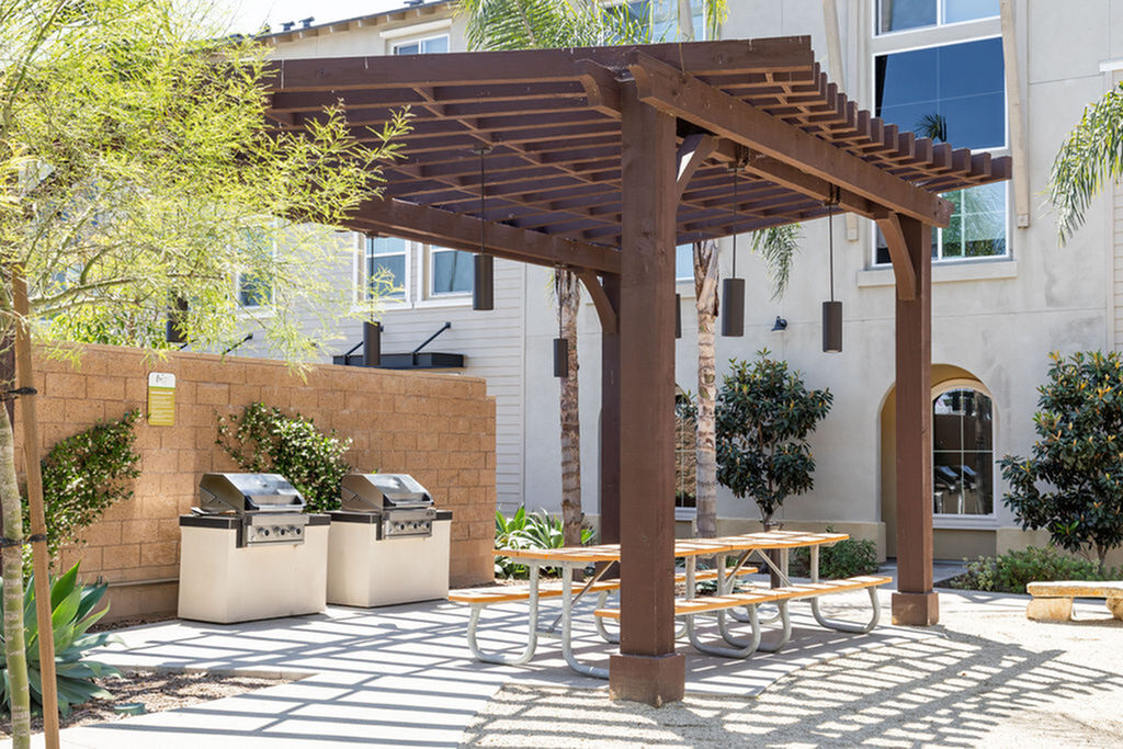 Inviting outdoor patio with wooden pergola and modern barbecue grills, perfect for entertaining in a lush garden setting.