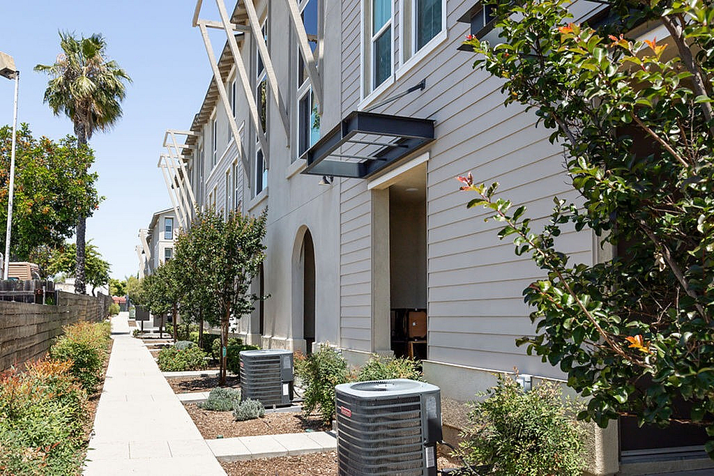 Modern apartment exterior with sleek design, abundant greenery, and spacious walkway, perfect for comfortable living.