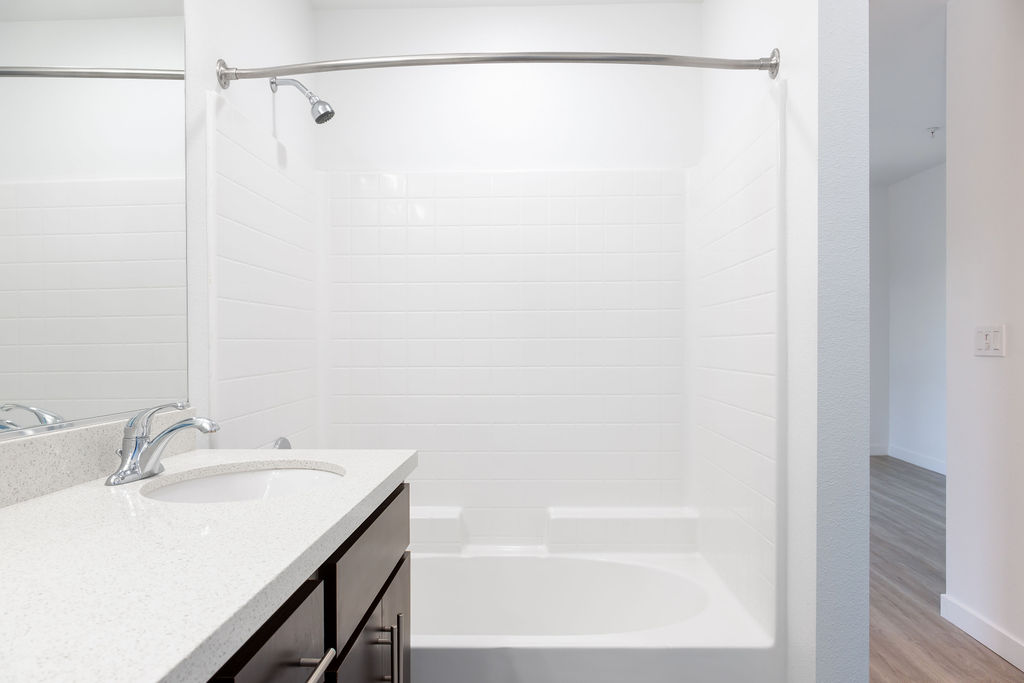 Modern bathroom with sleek white tiles, elegant vanity, and curved shower rod in a spacious apartment.