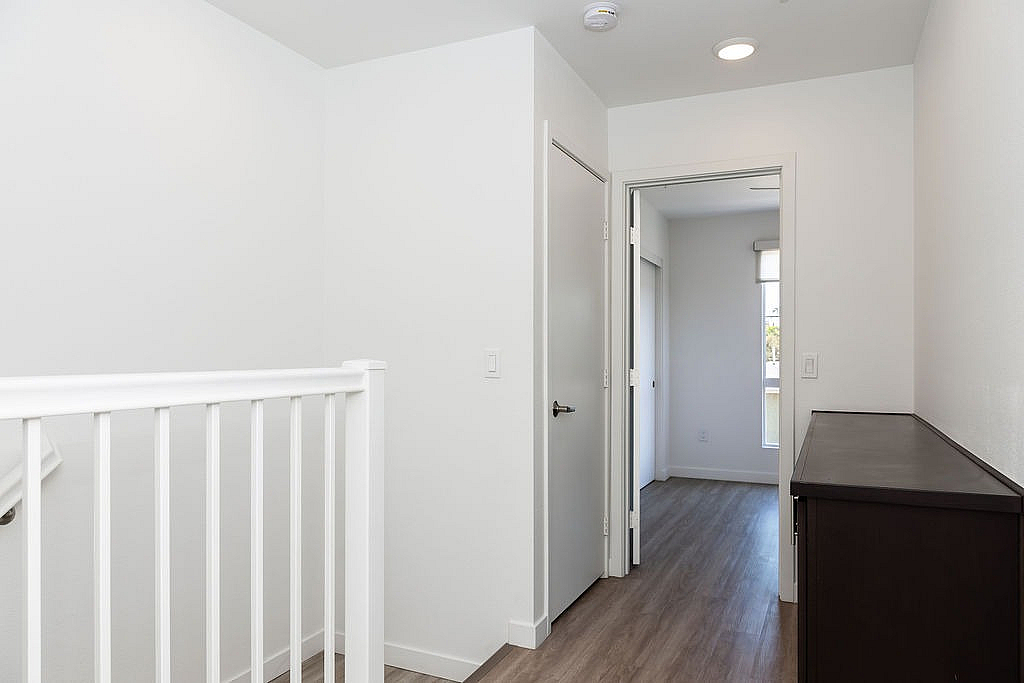 Bright and airy hallway with a wooden dresser, leading to a sunlit room with contemporary design.