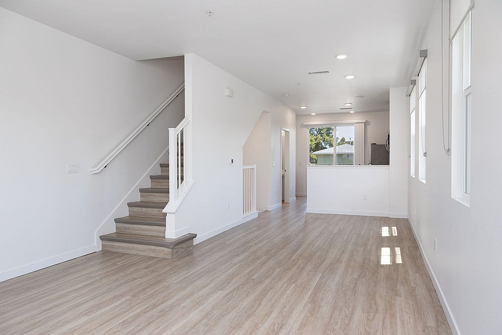 Bright and modern open-plan living area with sleek hardwood floors and a contemporary staircase, filled with natural light from multiple windows.