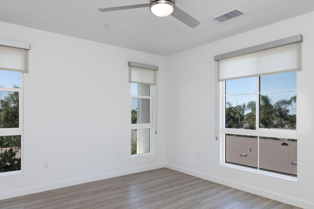 Bright bedroom with large windows and wood flooring, offering a serene view of palm trees.