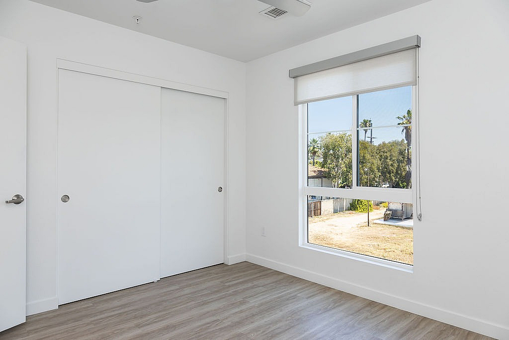 Bright, minimalist room with wood flooring, large window offering a serene view, and spacious white closet.