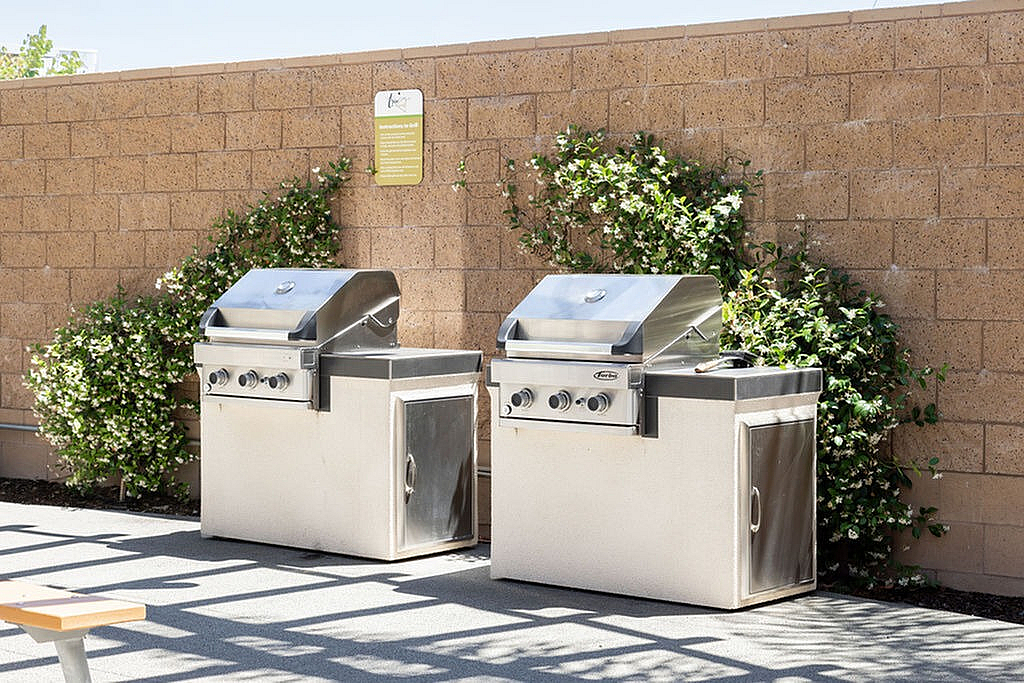 Outdoor cooking station featuring modern stainless steel grills set against a stylish brick wall with lush greenery.