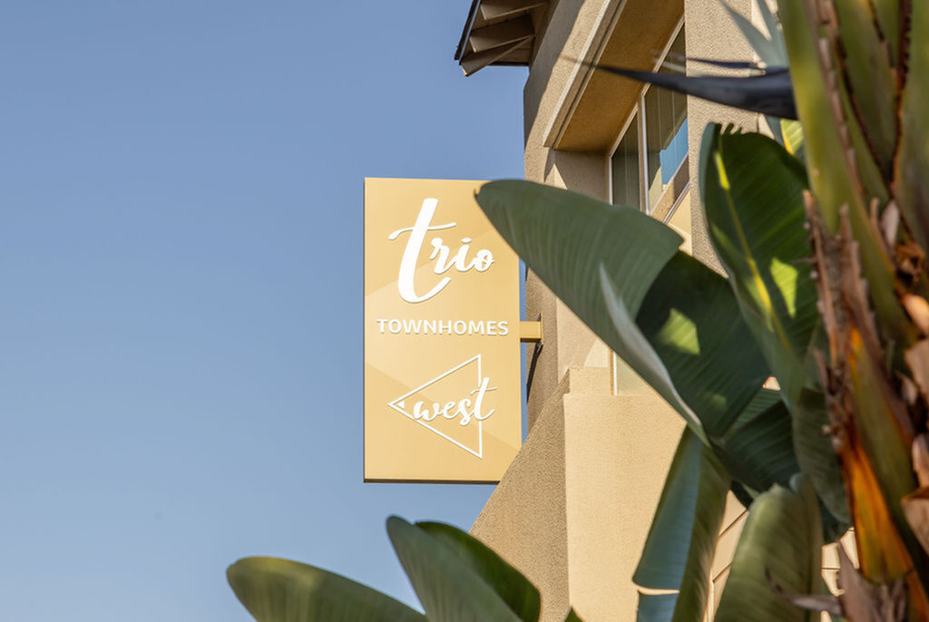 Inviting exterior view of Trio Townhomes with lush greenery and welcoming signage.