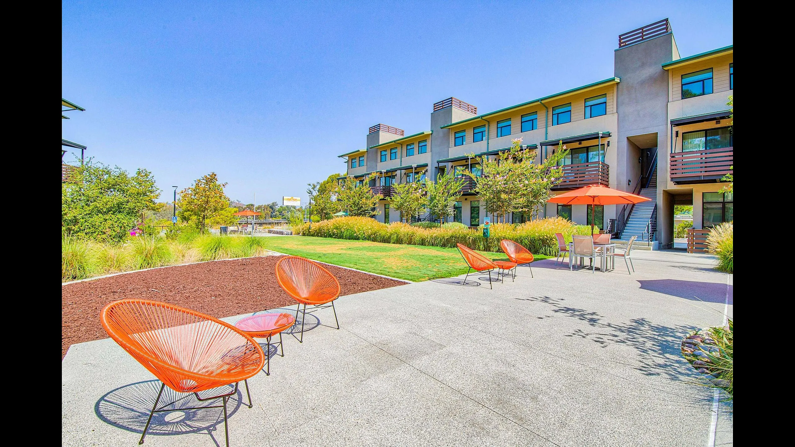 Warm sunny day showcasing modern apartment complex with vibrant landscaping and stylish outdoor seating.