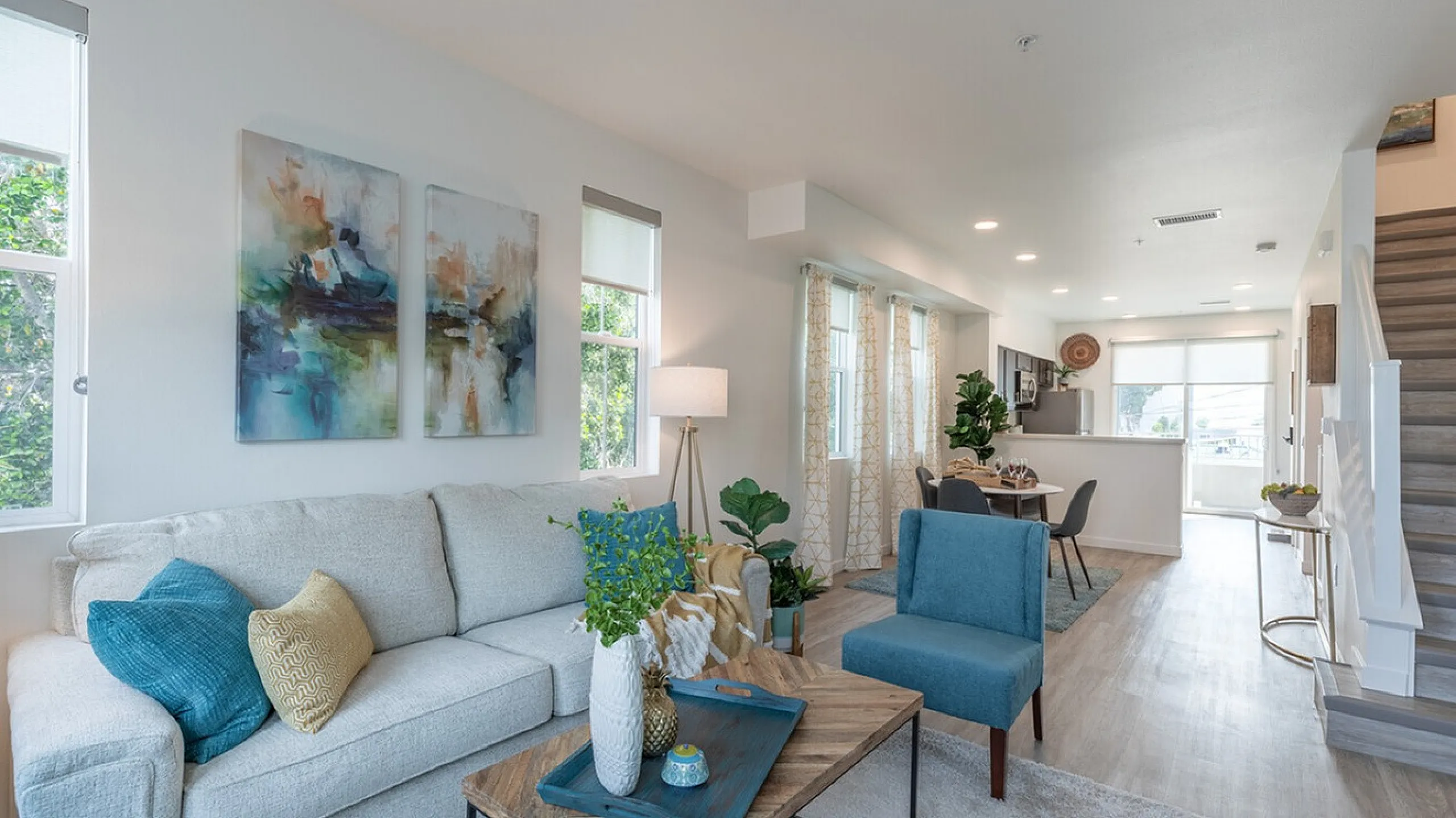 Modern living room with elegant decor, featuring a cozy beige sofa, vibrant artwork, and a sleek open-concept dining area.