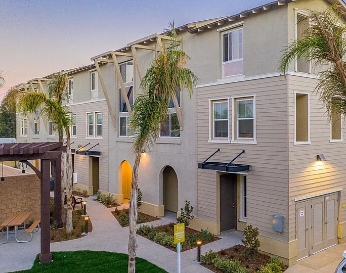 Contemporary townhomes featuring elegant architecture with large windows, a beautifully landscaped courtyard, and welcoming entryways under a twilight sky.