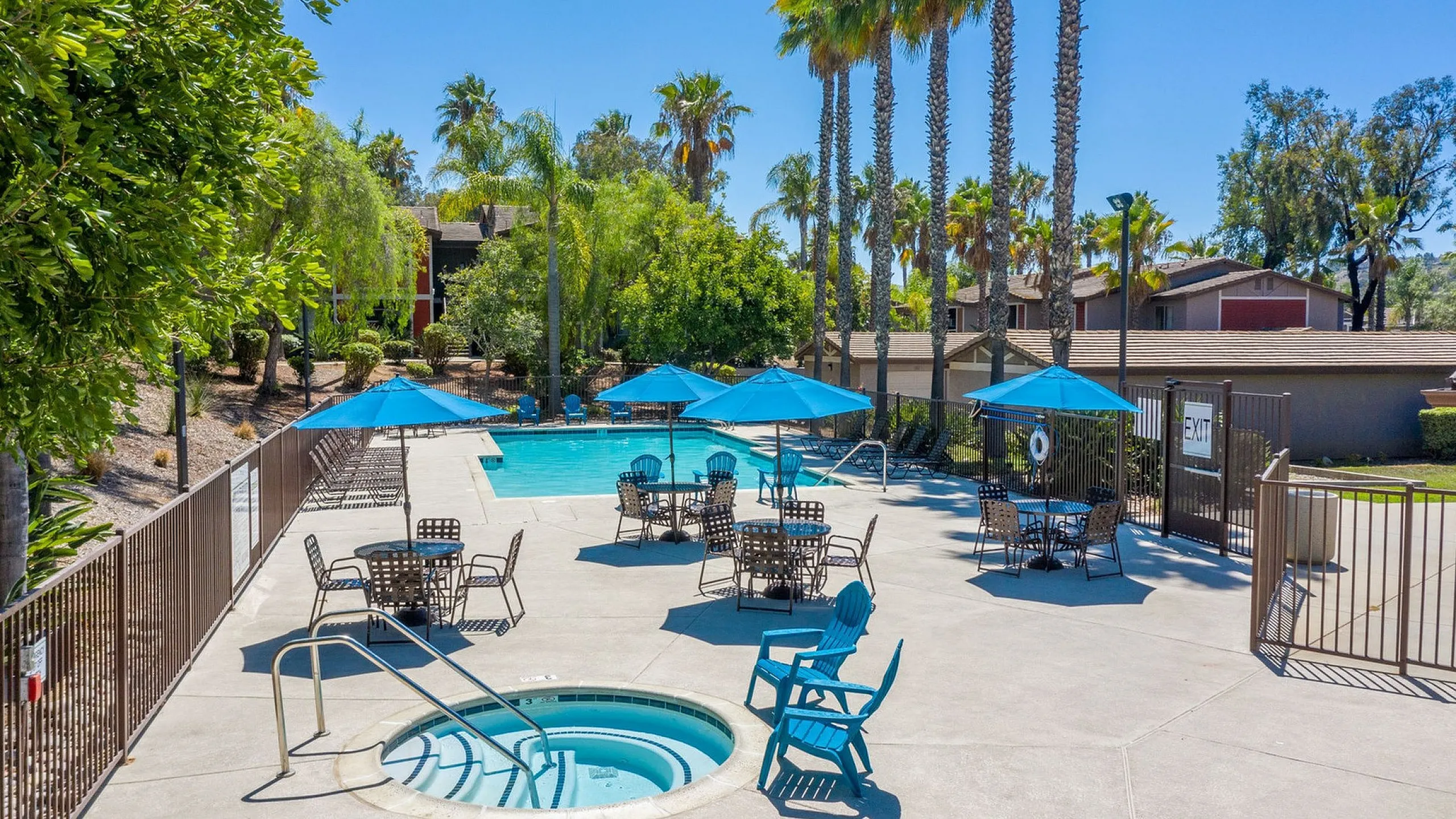 Inviting outdoor pool area with sunlit seating, vibrant blue umbrellas, and lush greenery creating a tropical oasis.