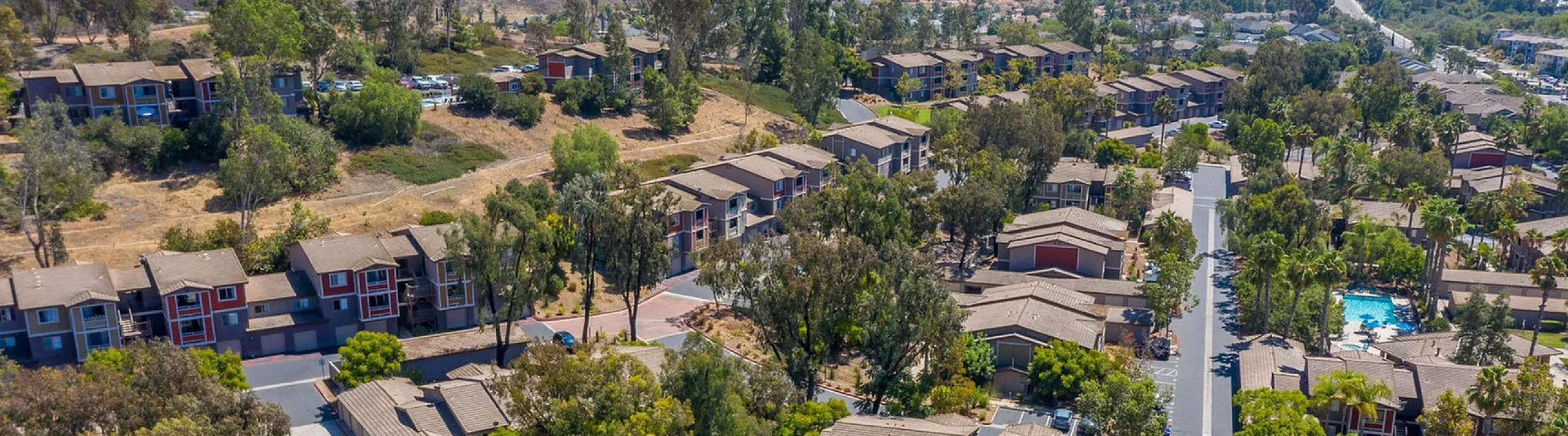 Aerial view of a serene residential community nestled among rolling hills, featuring charming homes, lush greenery, and a refreshing pool.