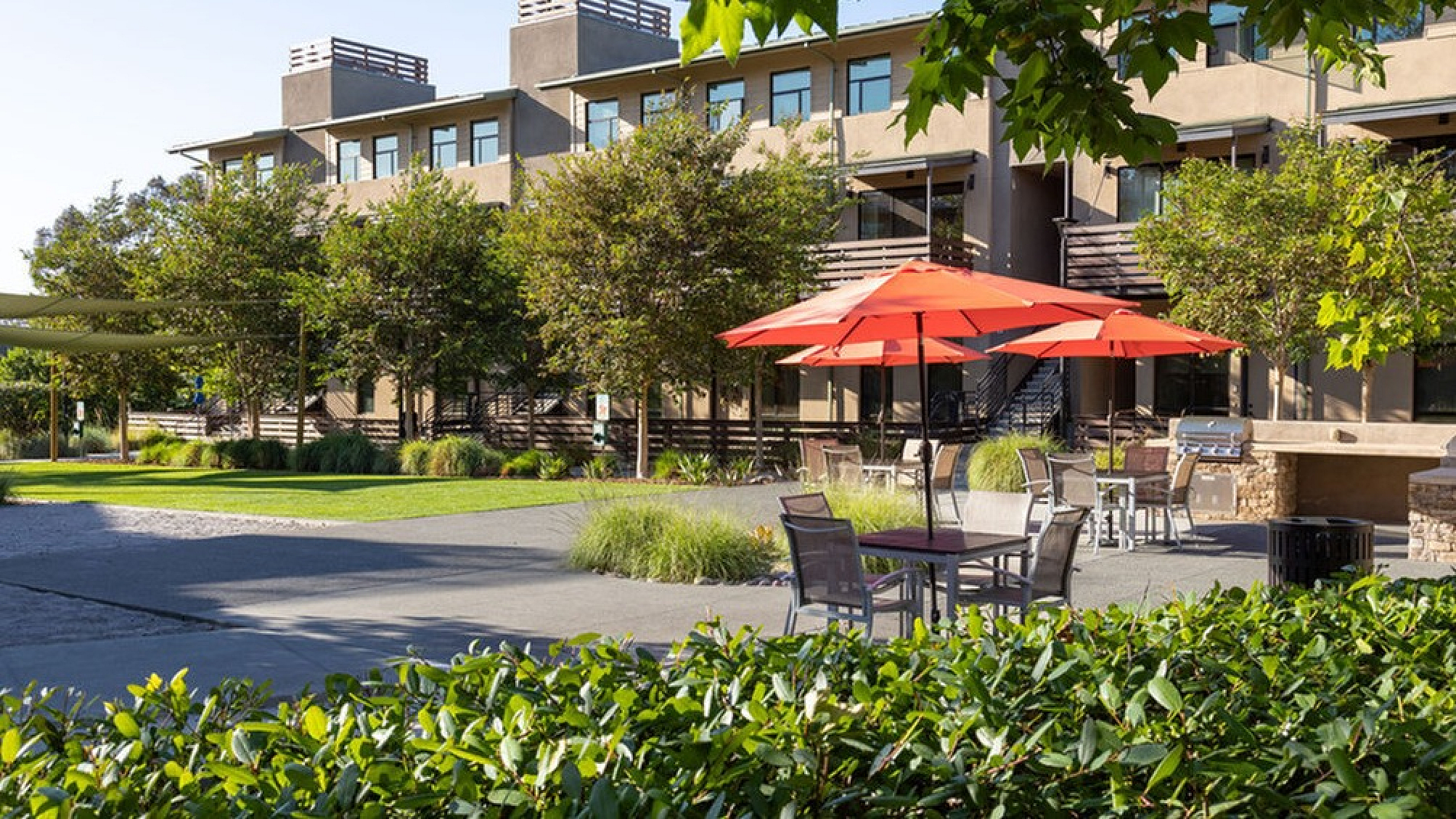 Charming courtyard with vibrant red umbrellas, lush greenery, and contemporary apartment facades offering outdoor relaxation.