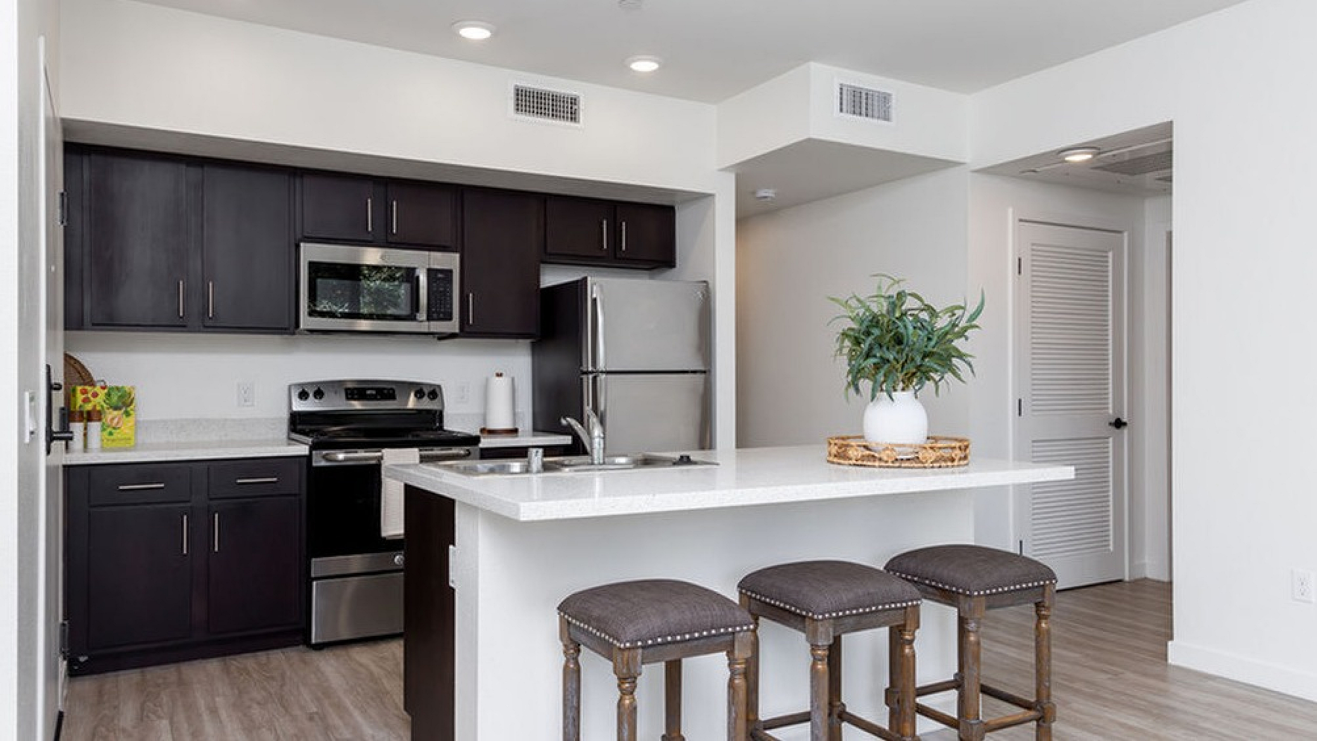 Modern kitchen with sleek dark cabinetry, stainless steel appliances, and a bright breakfast bar complemented by stylish bar stools.