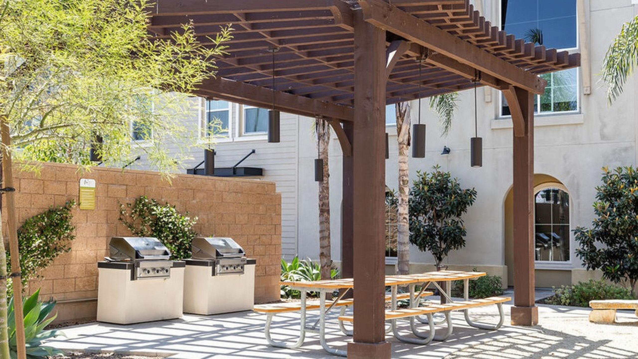 Charming outdoor patio with a wooden pergola, stylish picnic table, and modern stainless steel grills, perfect for entertaining.