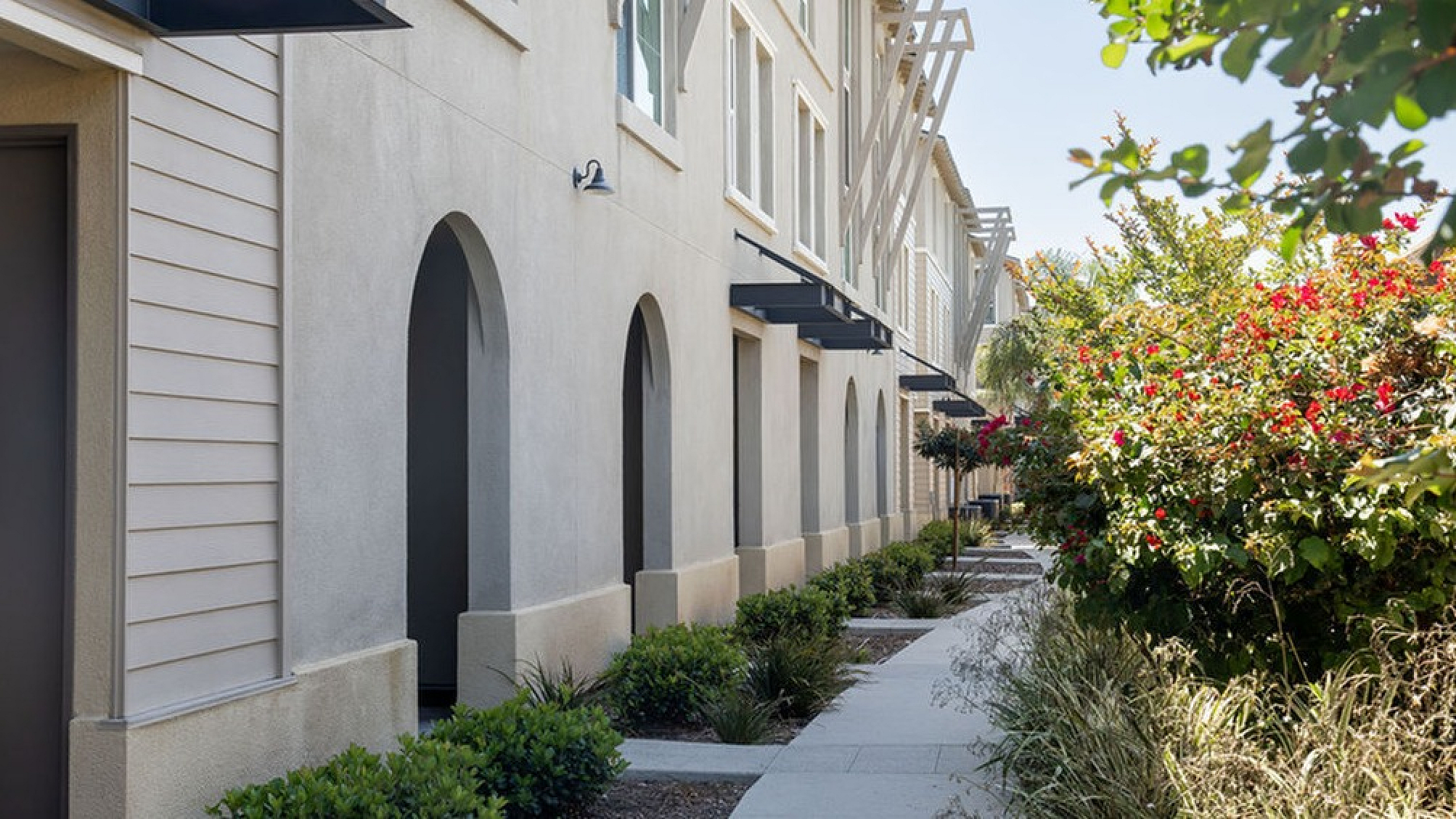 Charming townhome exterior with elegant arched windows, surrounded by lush gardens and a welcoming walkway.
