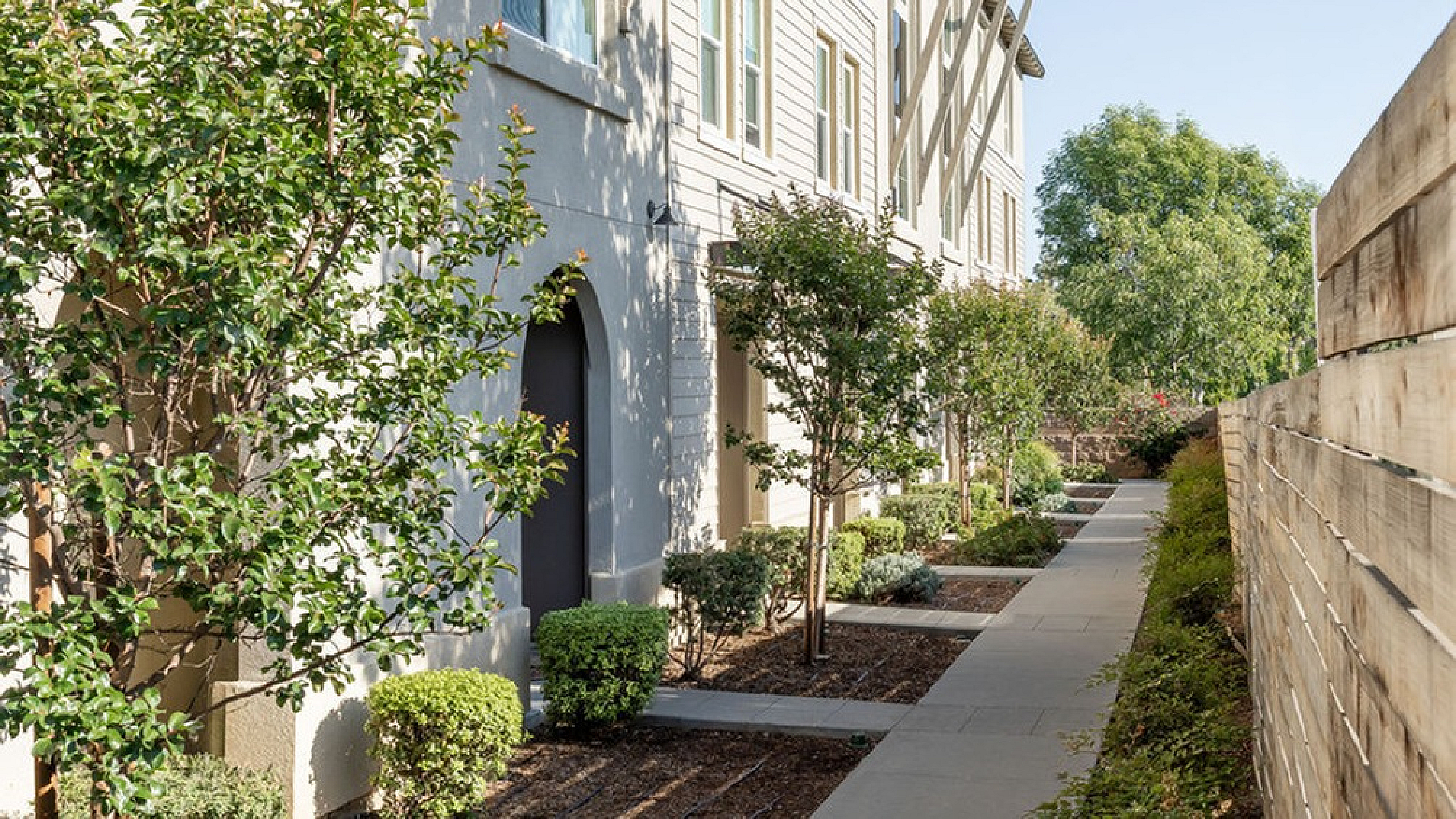 Charming apartment exterior with lush greenery, modern architecture, and a sunlit pathway.