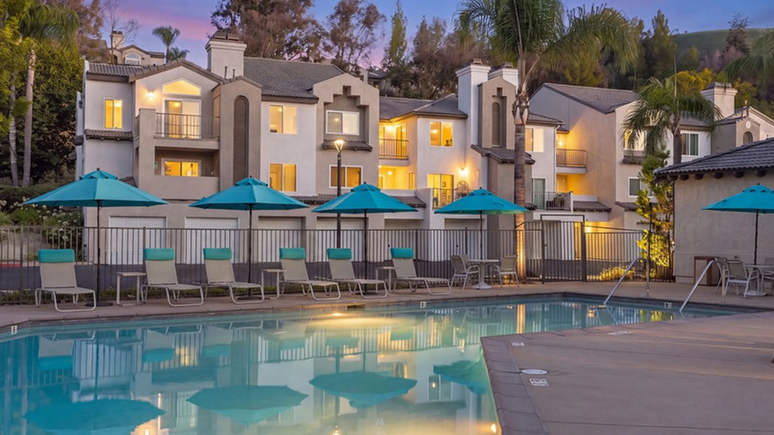 Elegant apartment community with a sparkling pool, surrounded by lush palm trees and vibrant sunsets.