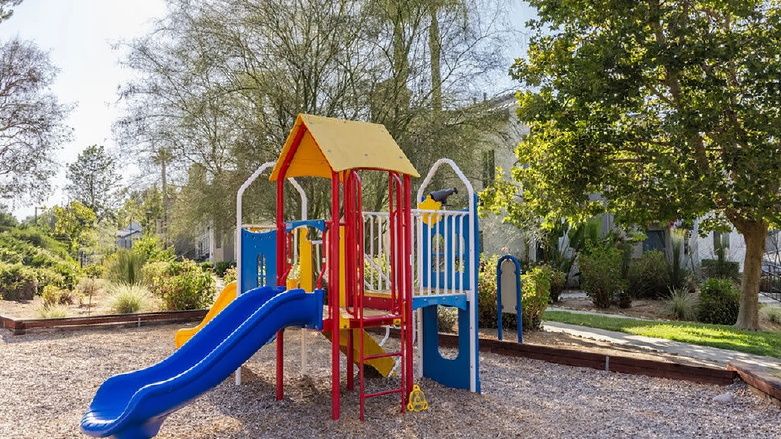 Charming outdoor playground with colorful slides and structures, surrounded by lush greenery and trees.