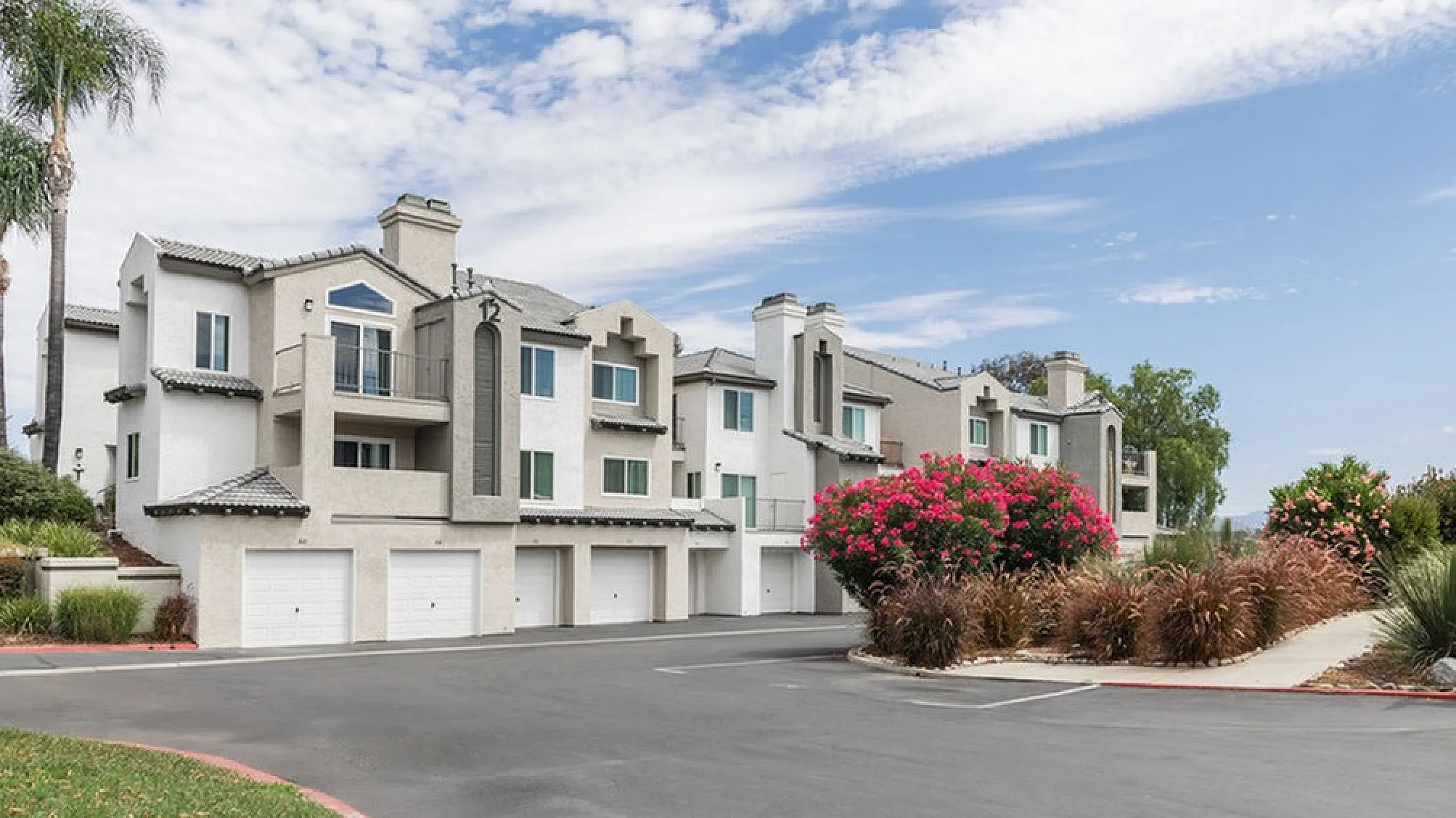 Charming multi-story residential community with modern architecture, lush landscaping, and attached garages under a clear blue sky.