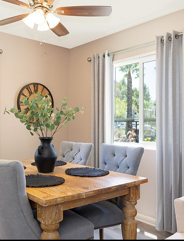 Bright dining area with elegant wooden table, plush gray chairs, and large windows offering scenic outdoor views.