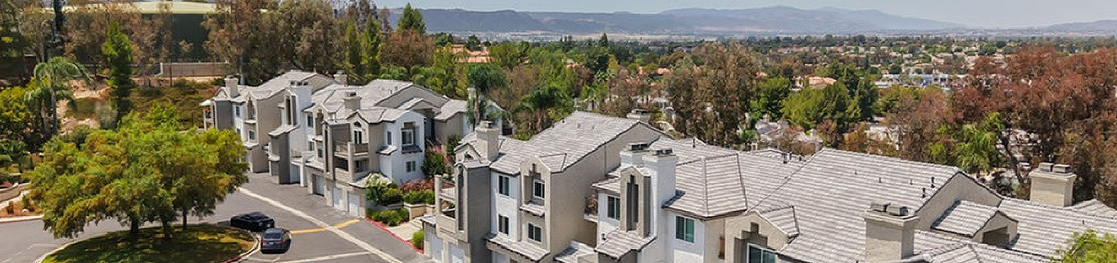 Aerial view of a picturesque suburban apartment surrounded by lush greenery and set against scenic rolling hills.