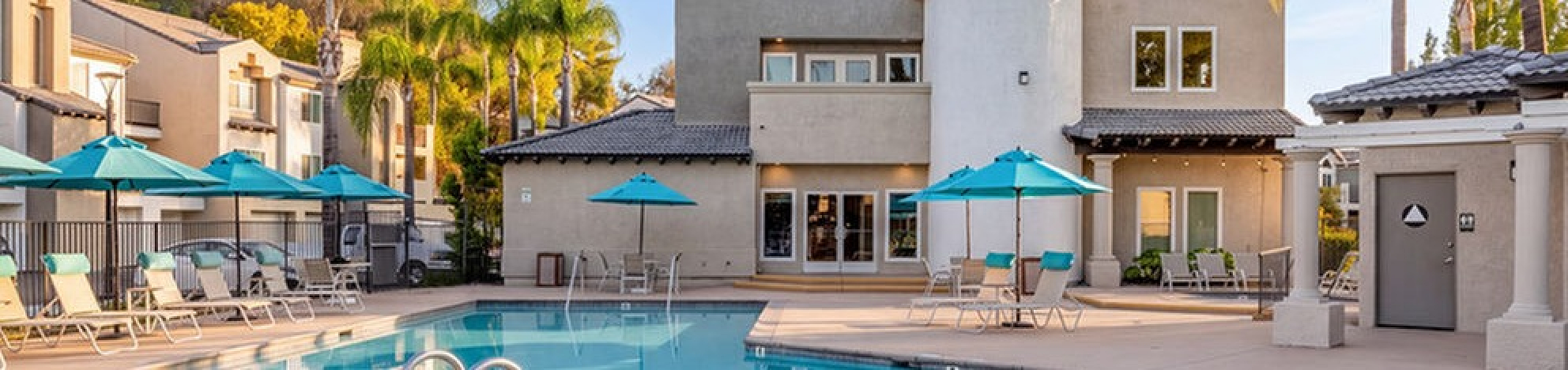 Luxurious apartment community pool surrounded by stylish lounge chairs and vibrant palm trees, perfect for relaxing under the sunny skies.