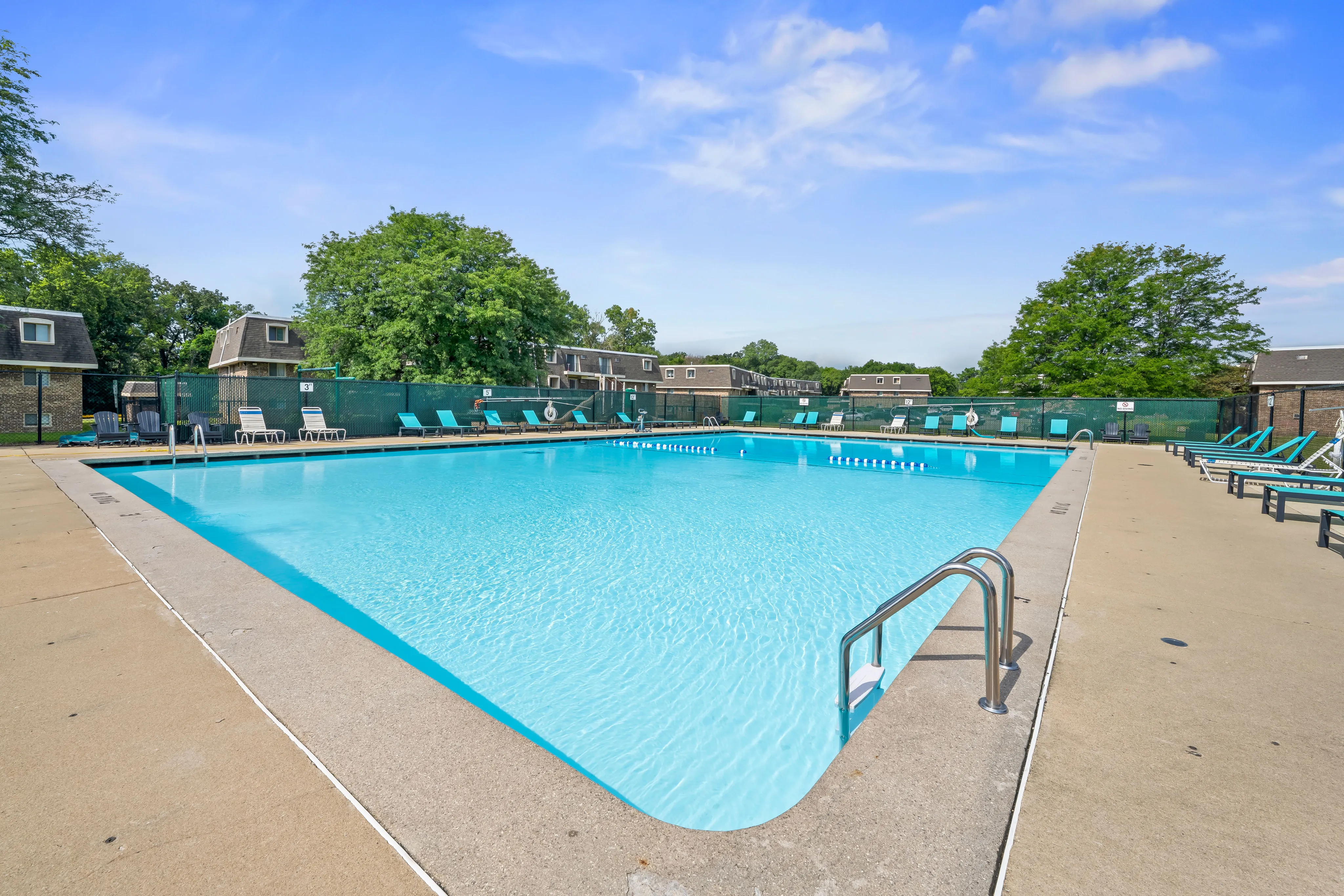 Inviting outdoor pool area with bright blue water, surrounded by sun loungers and lush greenery under a clear sky.