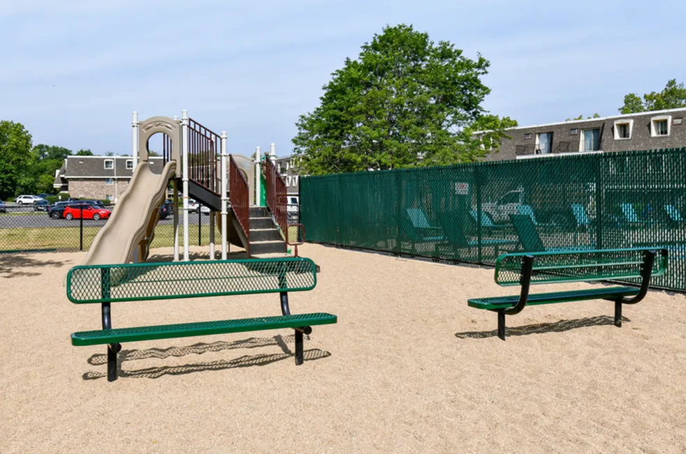 Inviting playground area with slide and benches, surrounded by lush greenery and modern apartments.