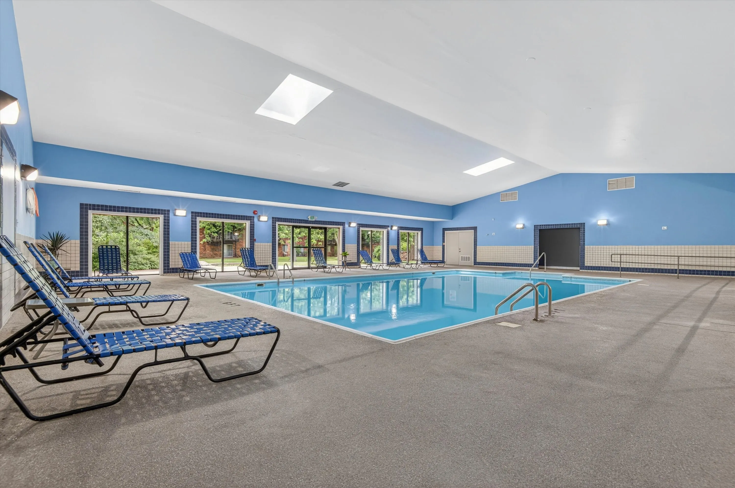Inviting indoor pool area with comfortable blue lounge chairs, large skylights, and a serene atmosphere perfect for relaxation.