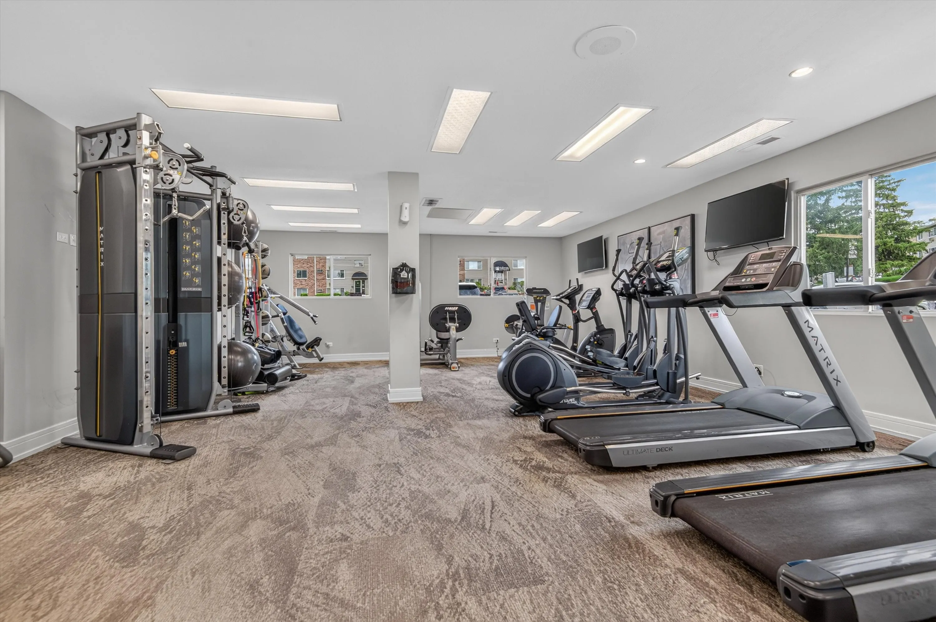 Modern fitness center with state-of-the-art equipment, including treadmills, ellipticals, and a multi-functional machine, set in a bright and spacious room with stylish flooring.