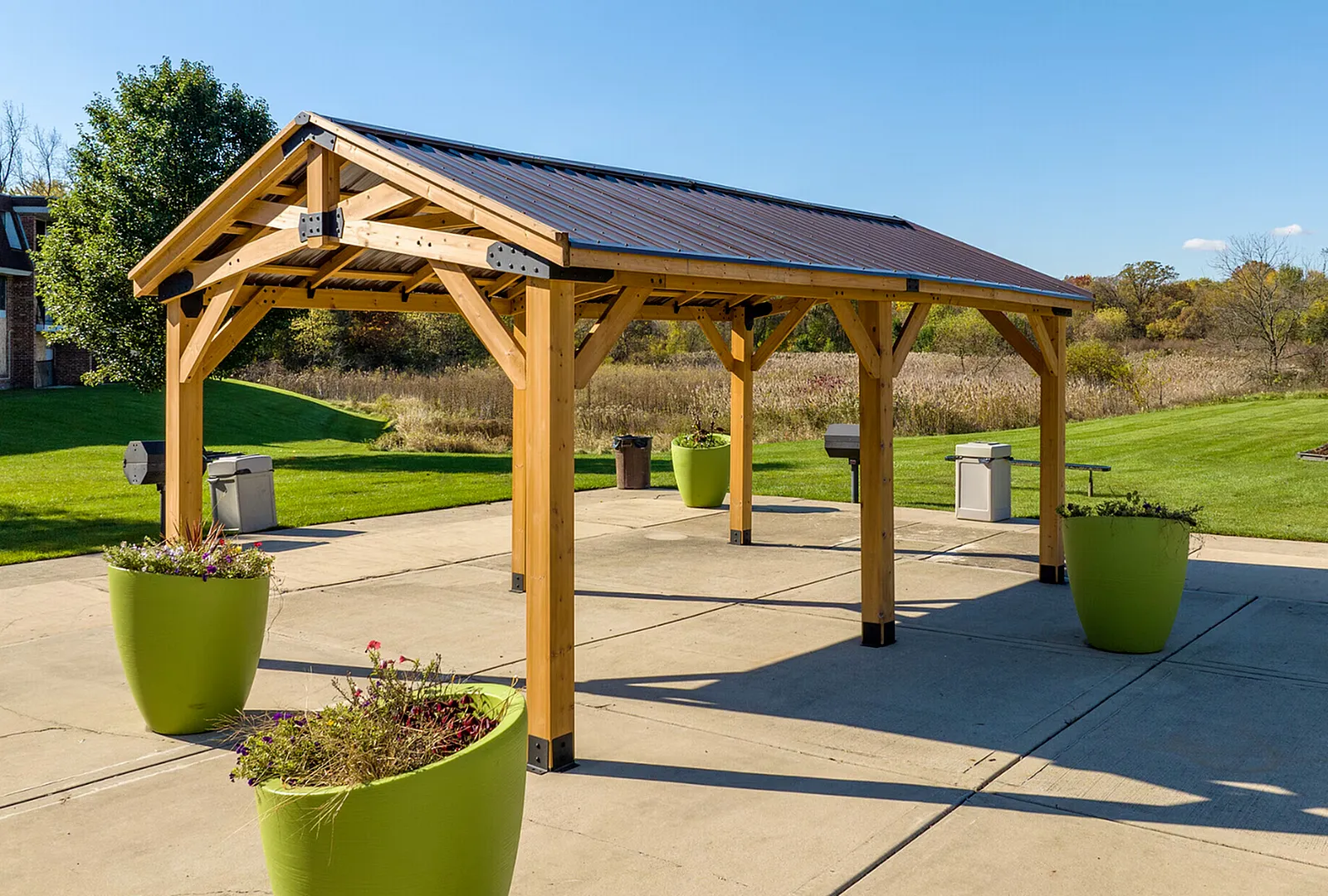 Charming outdoor gazebo with wooden construction, shaded sitting area, and vibrant green planters, set against a lush landscaped backdrop.