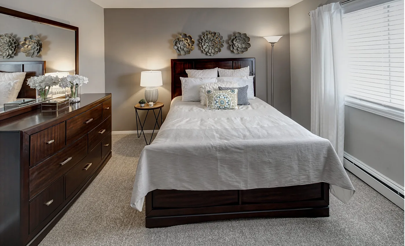 Inviting bedroom featuring a cozy bed with elegant linens, stylish wooden dresser, and tasteful decor under soft natural light.