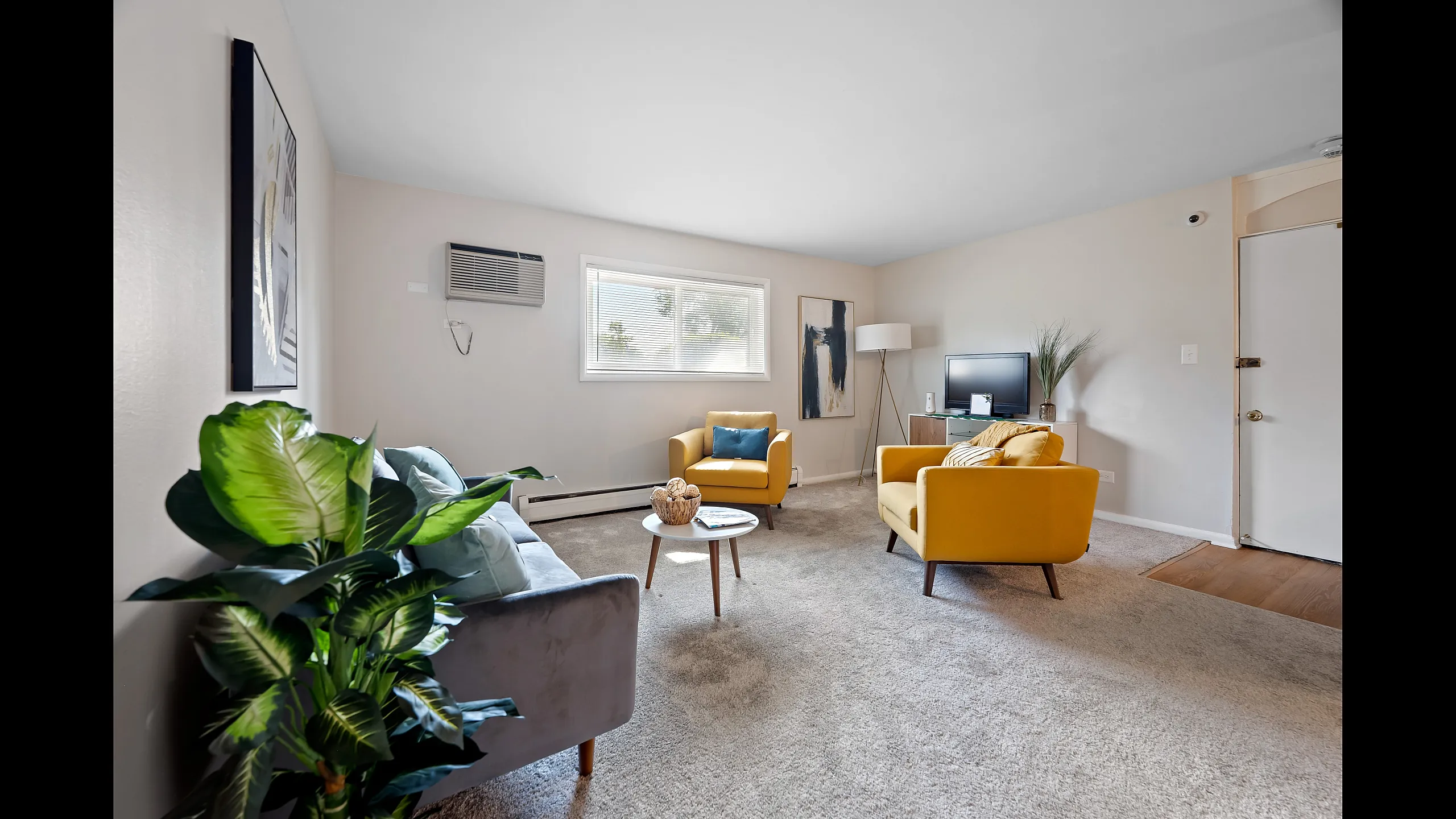 Bright and inviting living room with modern decor, featuring cozy yellow chairs, a stylish gray sofa, and vibrant green plants.