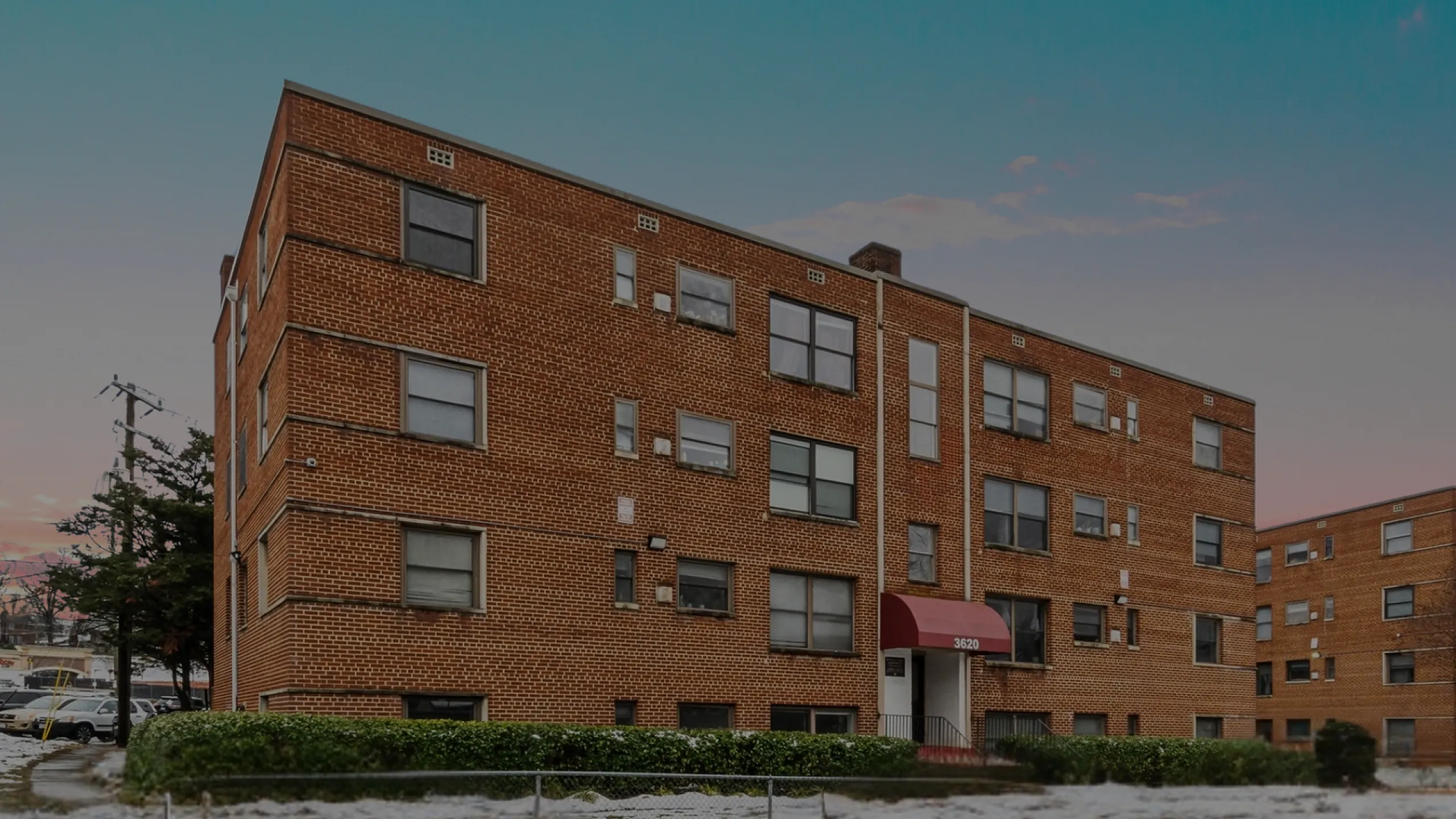 A classic brick apartment building with multiple stories and large windows, set against a serene evening sky.