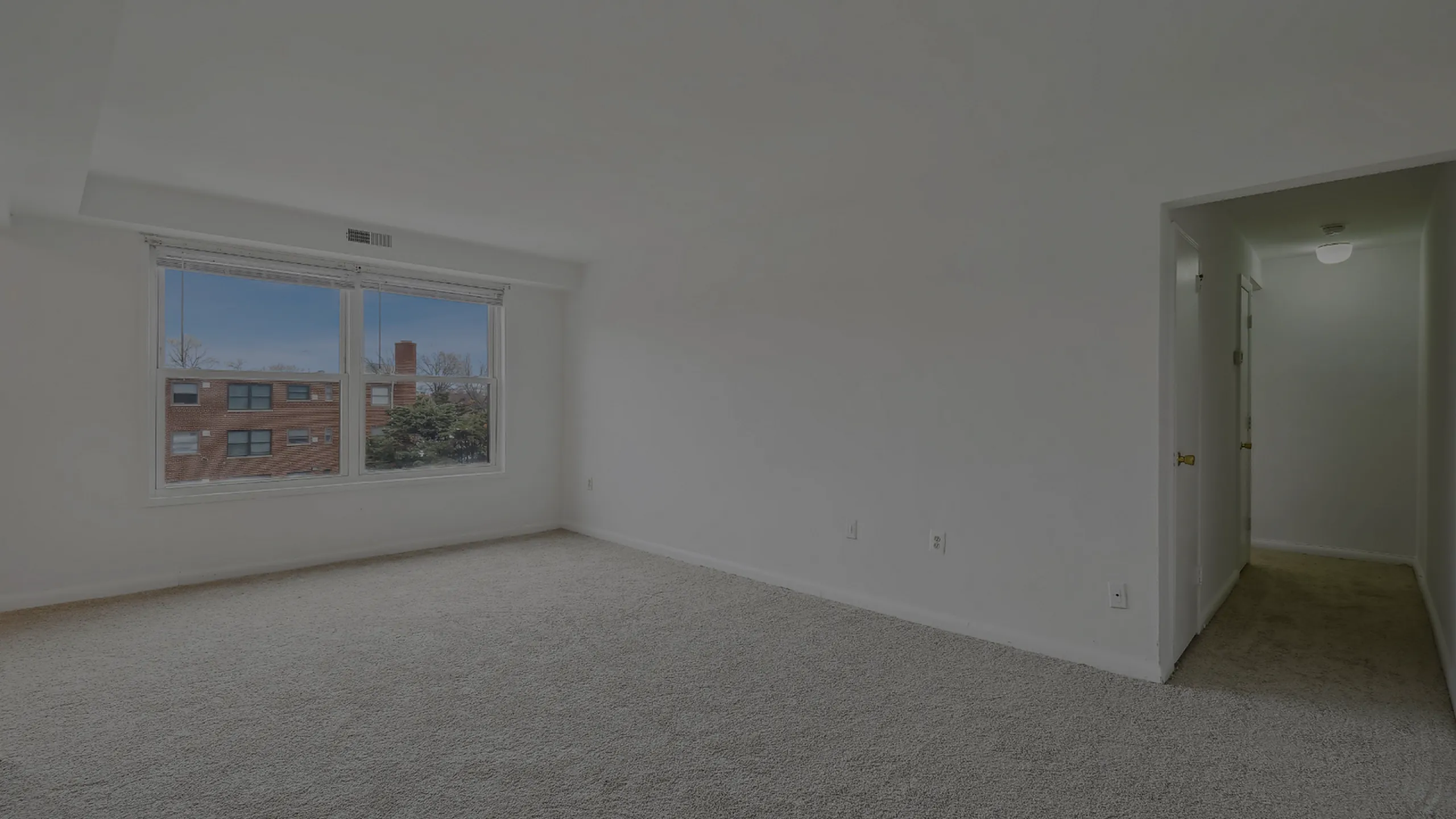 Spacious carpeted room with large window and hallway access.