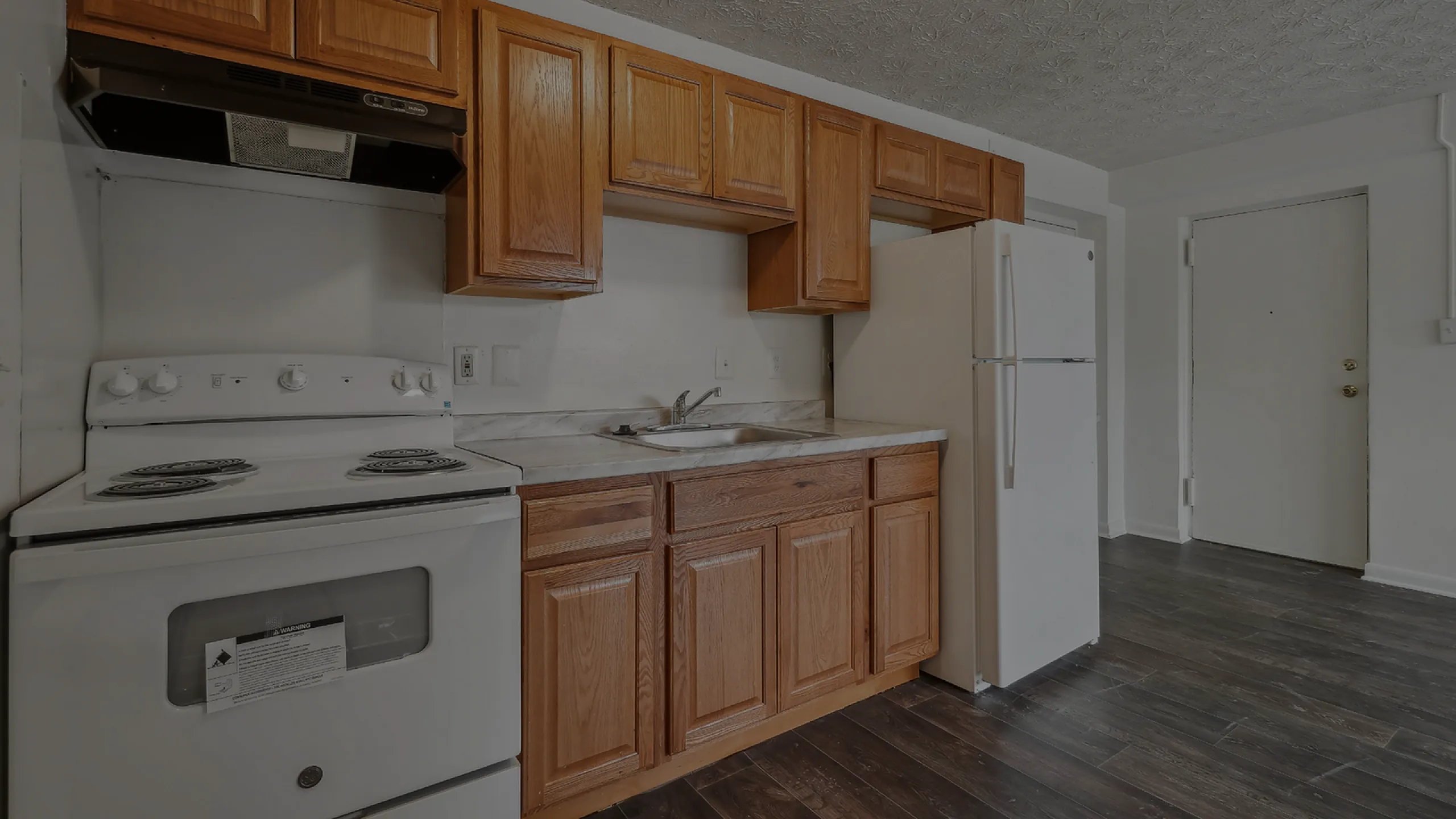 Inviting kitchen with wooden cabinetry, modern white appliances, and dark wood flooring.
