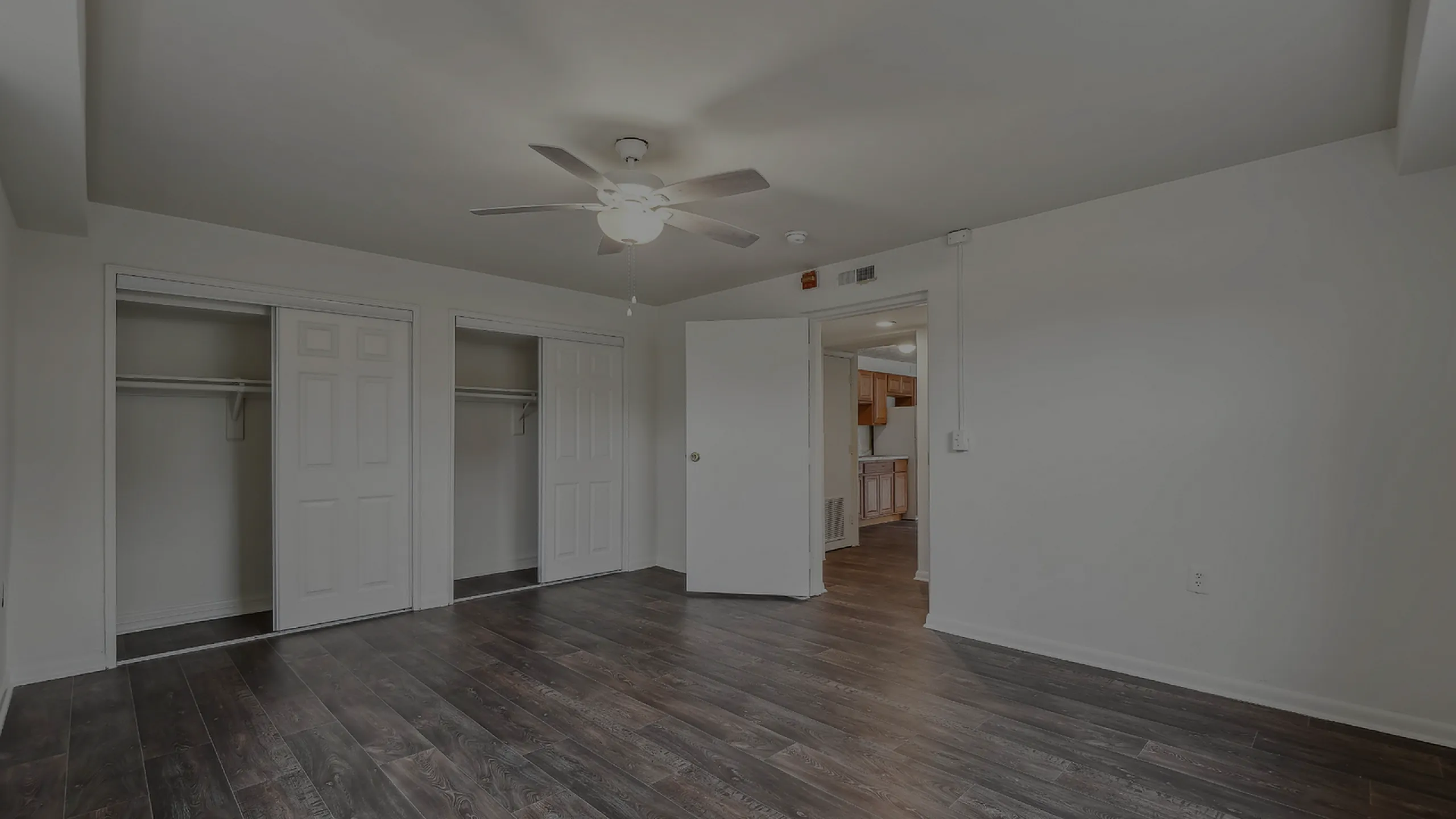 Spacious bedroom with wooden flooring, ceiling fan, and dual closets.
