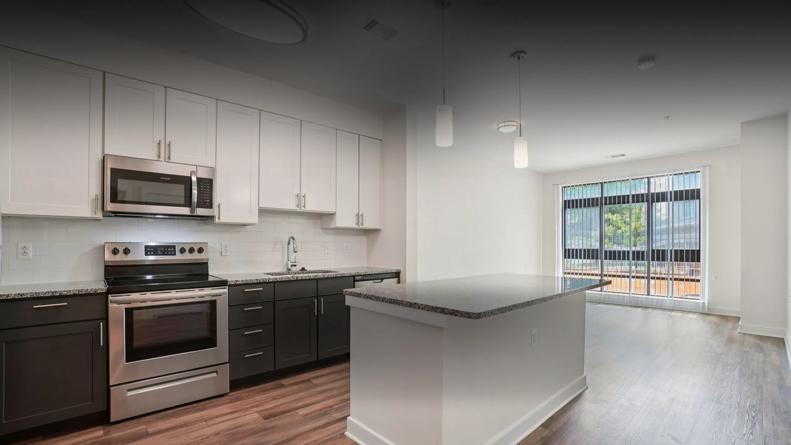 Modern kitchen with sleek stainless steel appliances, ample cabinetry, and a large island, opening to a bright living area with floor-to-ceiling windows.