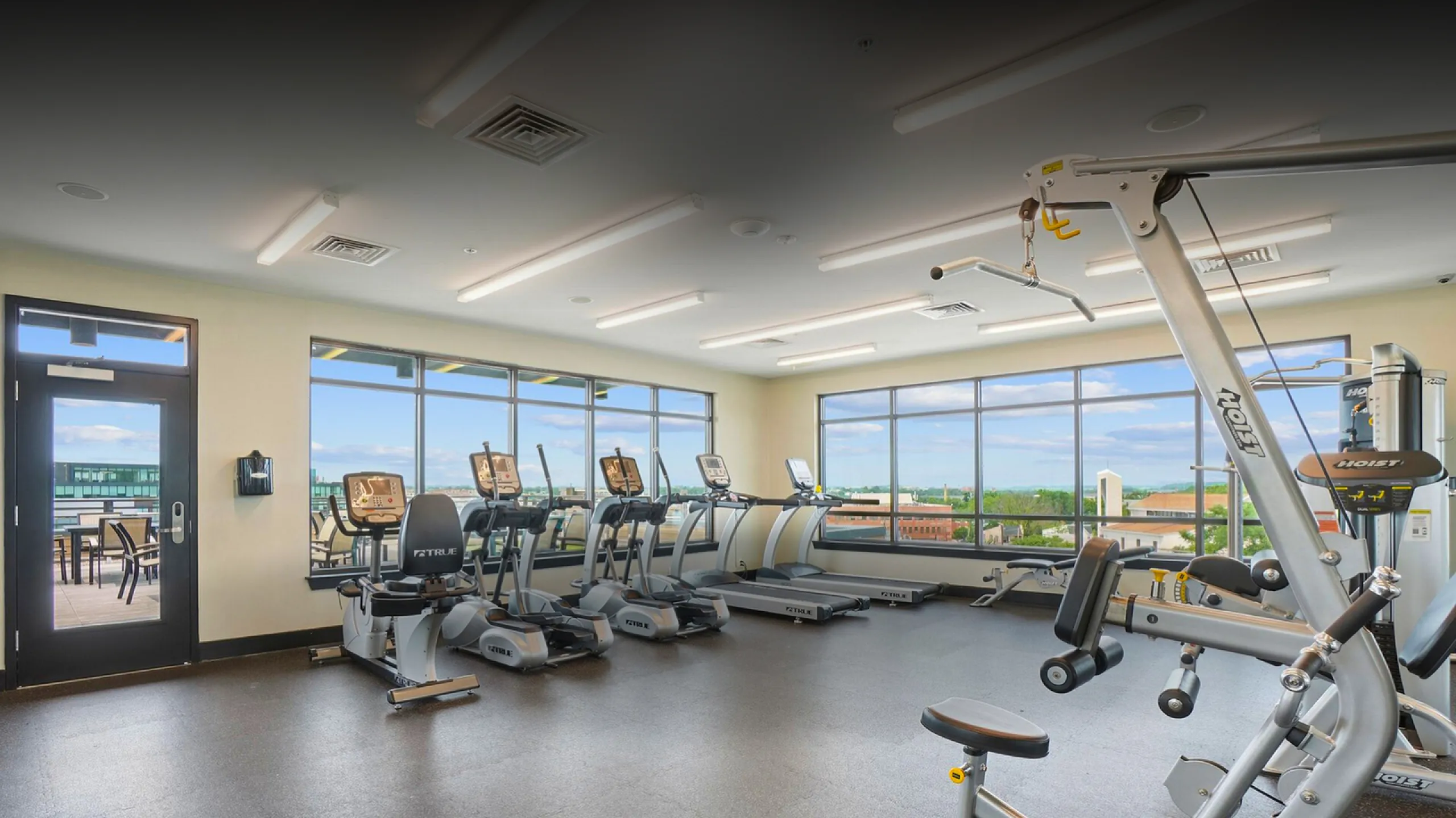 Bright and modern apartment gym with state-of-the-art equipment and scenic city views through large windows.
