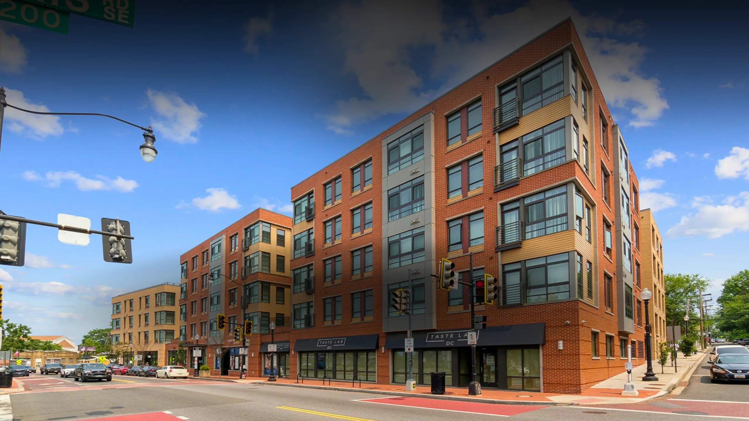 Contemporary urban apartment building with sleek brick facade and large windows, located at a bustling street corner.