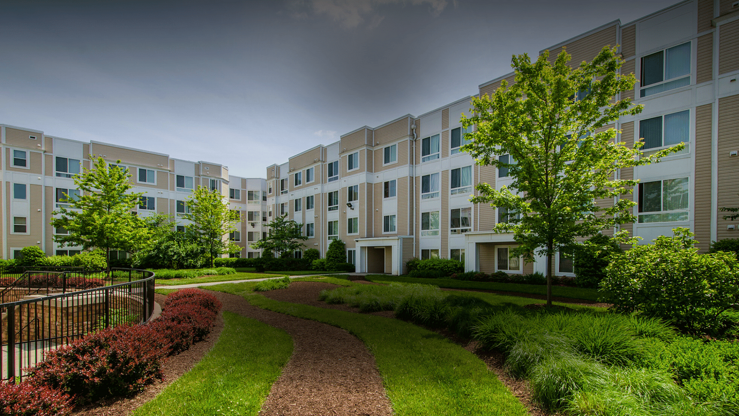 Charming four-story apartment building surrounded by lush greenery and manicured gardens, offering a peaceful residential ambiance.