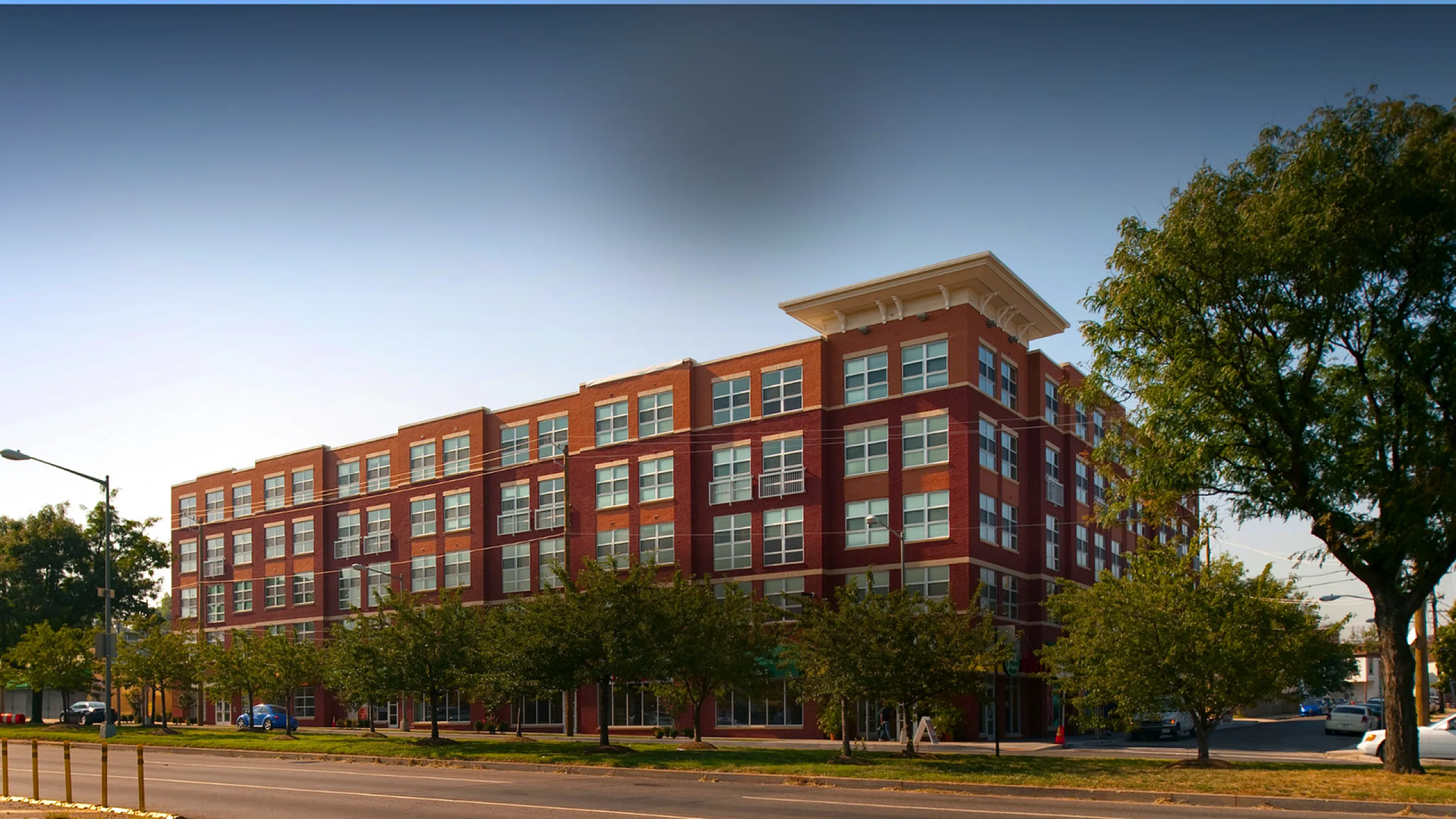 Modern red-brick apartment building with expansive windows and lush greenery, perfect for urban living.