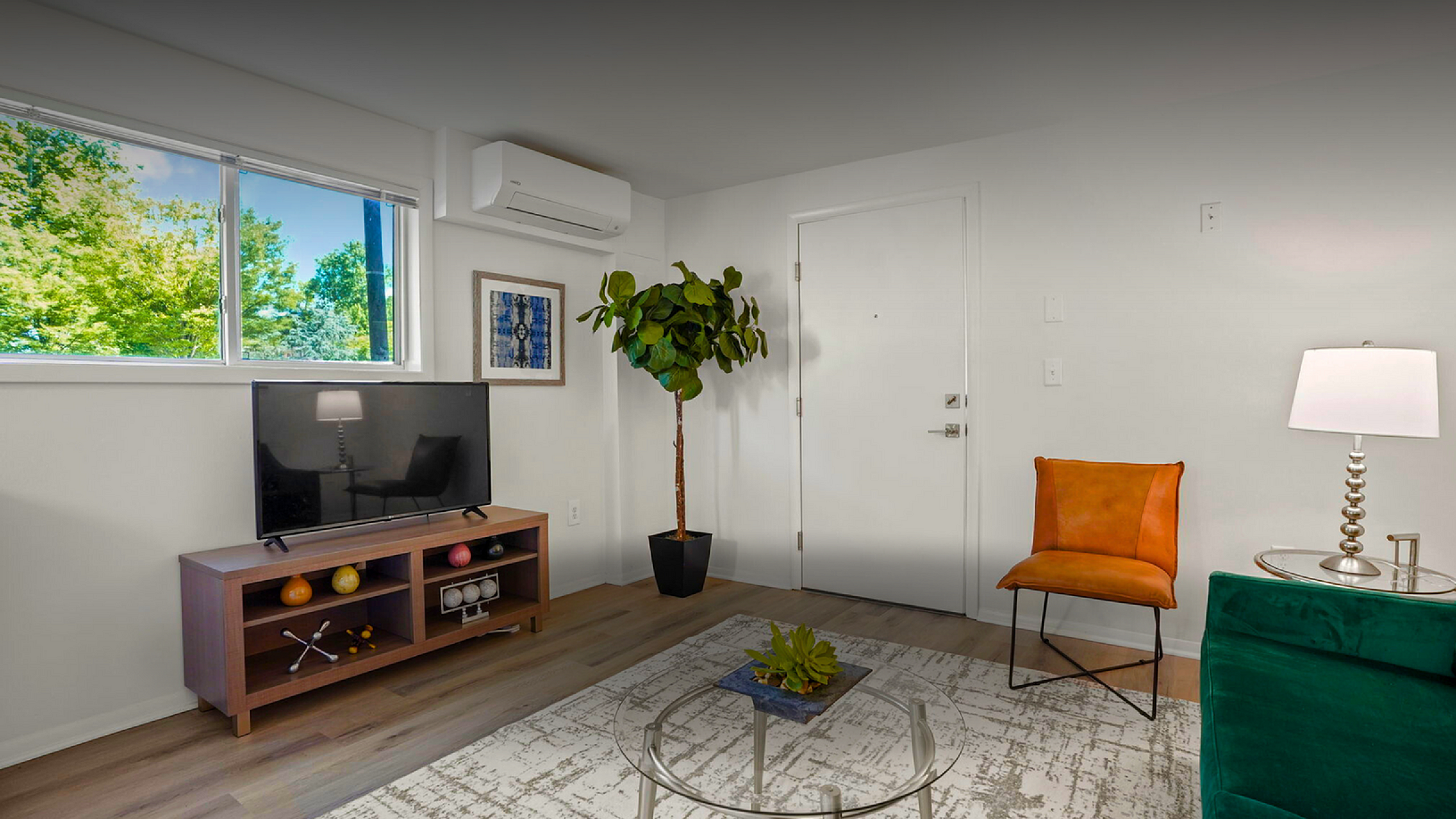 Bright and inviting living room with a modern TV setup, stylish decor, and large window showcasing lush greenery.