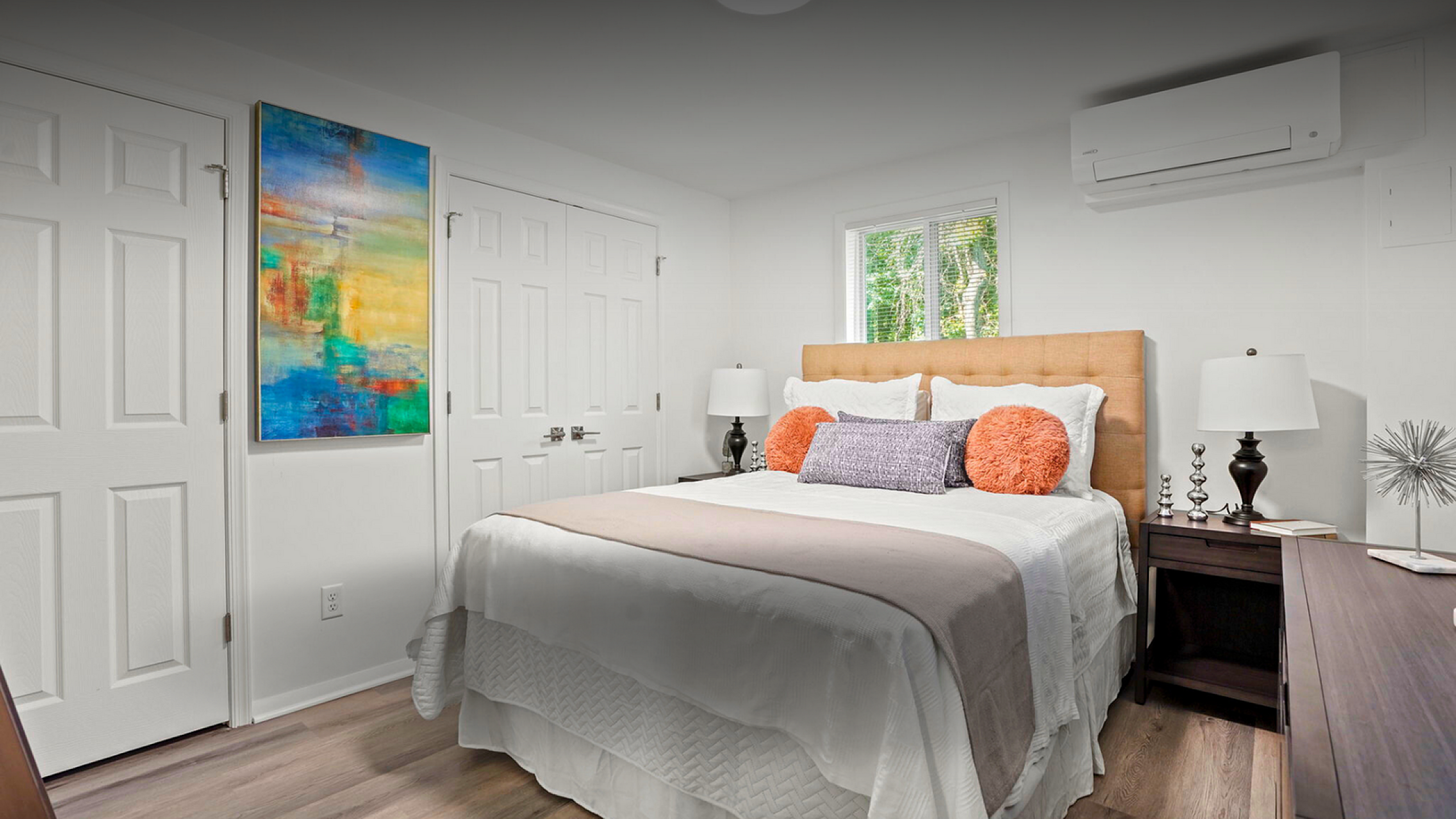 Cozy bedroom with modern decor featuring a plush bed, vibrant abstract artwork, and natural light from a scenic window view.