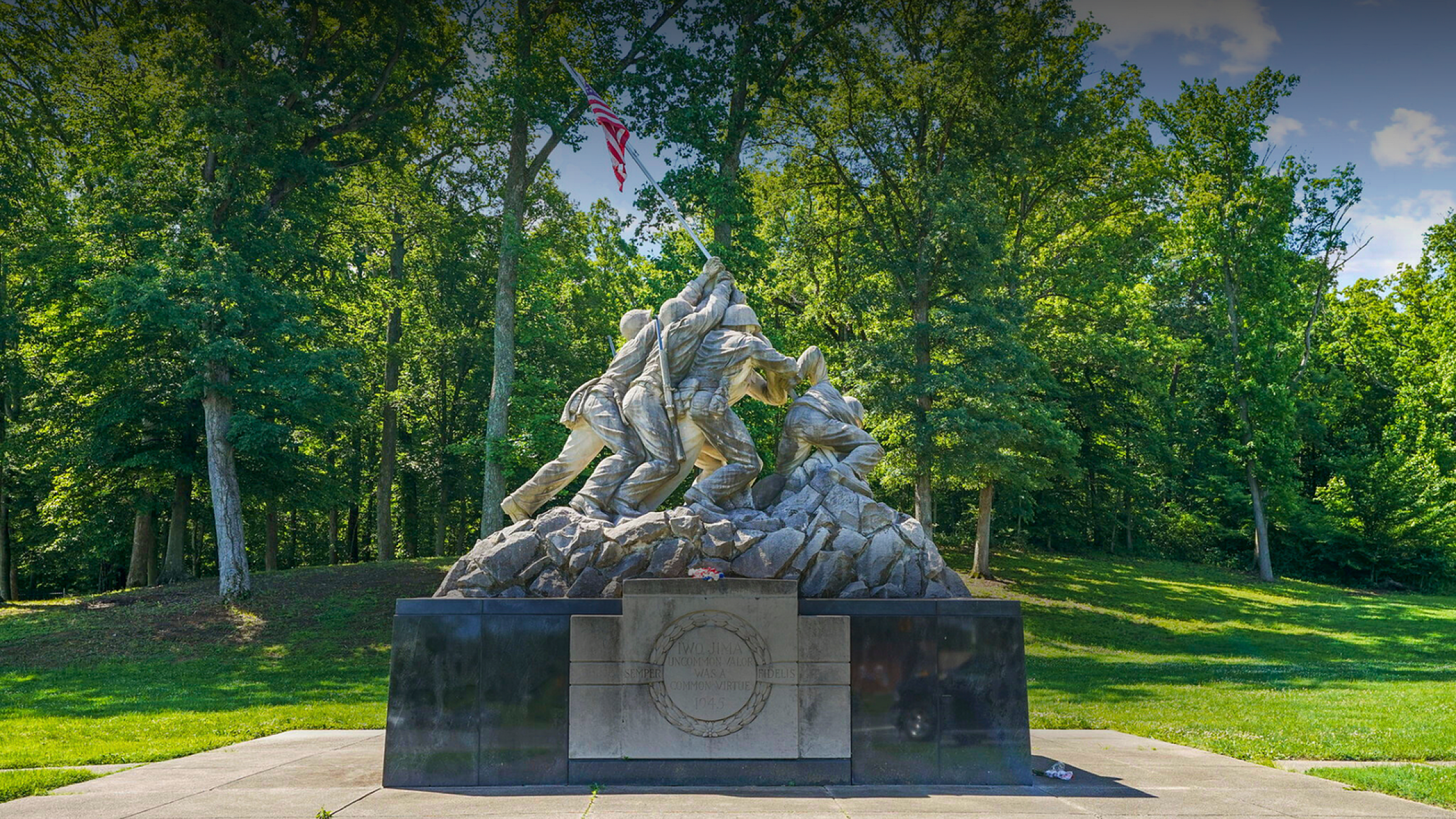 Majestic outdoor statue of soldiers raising a flag, surrounded by a lush green forest and clear blue sky.