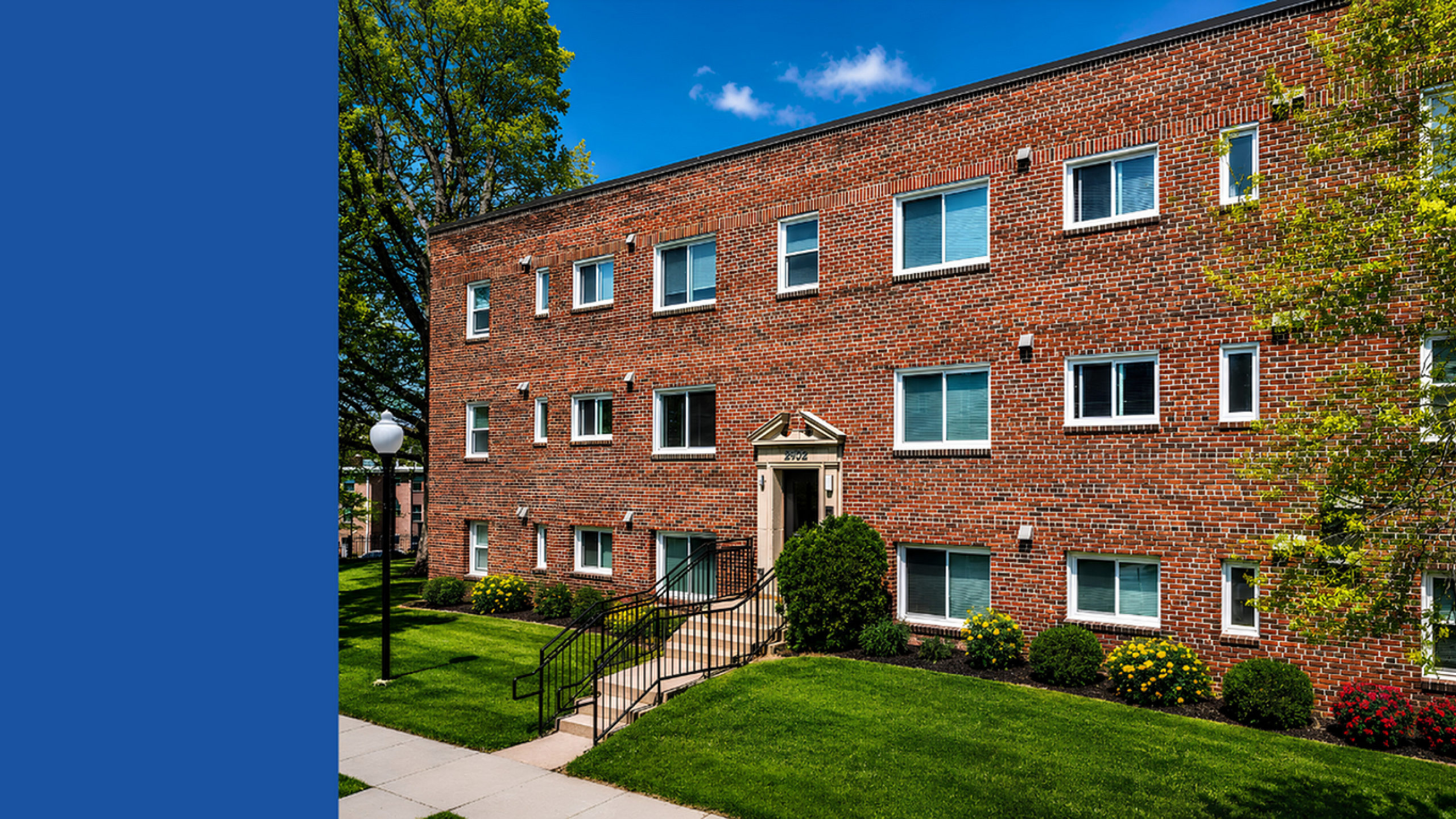 Charming brick apartment building with manicured landscaping and bright windows under a clear blue sky.