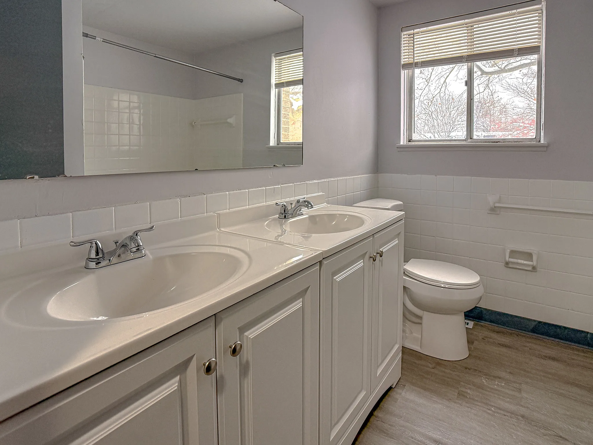 Bright and inviting bathroom with dual sinks, sleek countertops, and a large mirror, offering modern elegance.