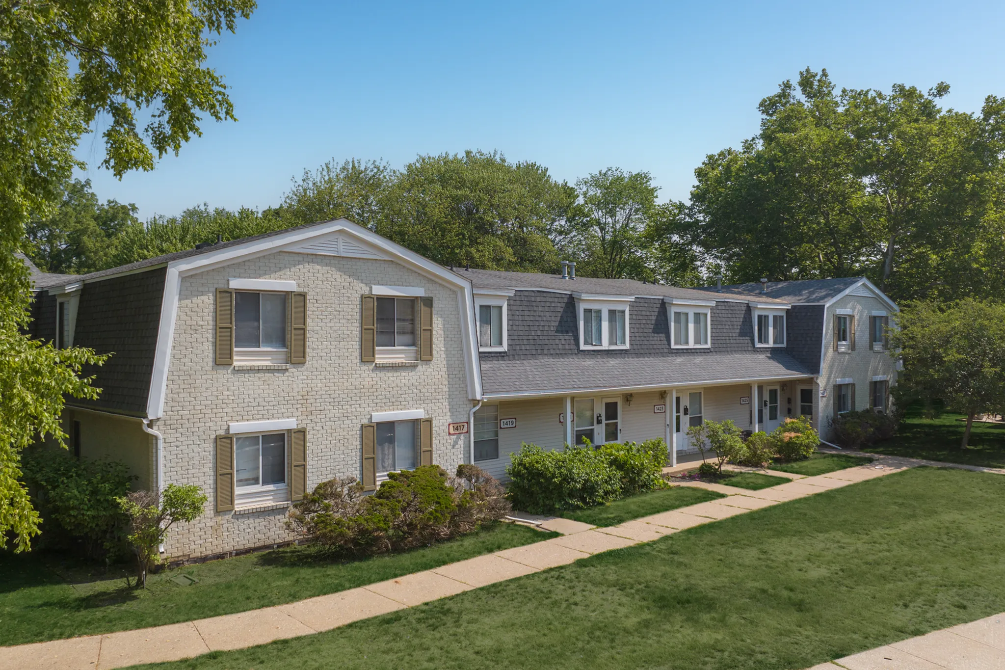 Charming multi-unit residential building surrounded by lush greenery, showcasing a classic architectural design with large windows and inviting paths.